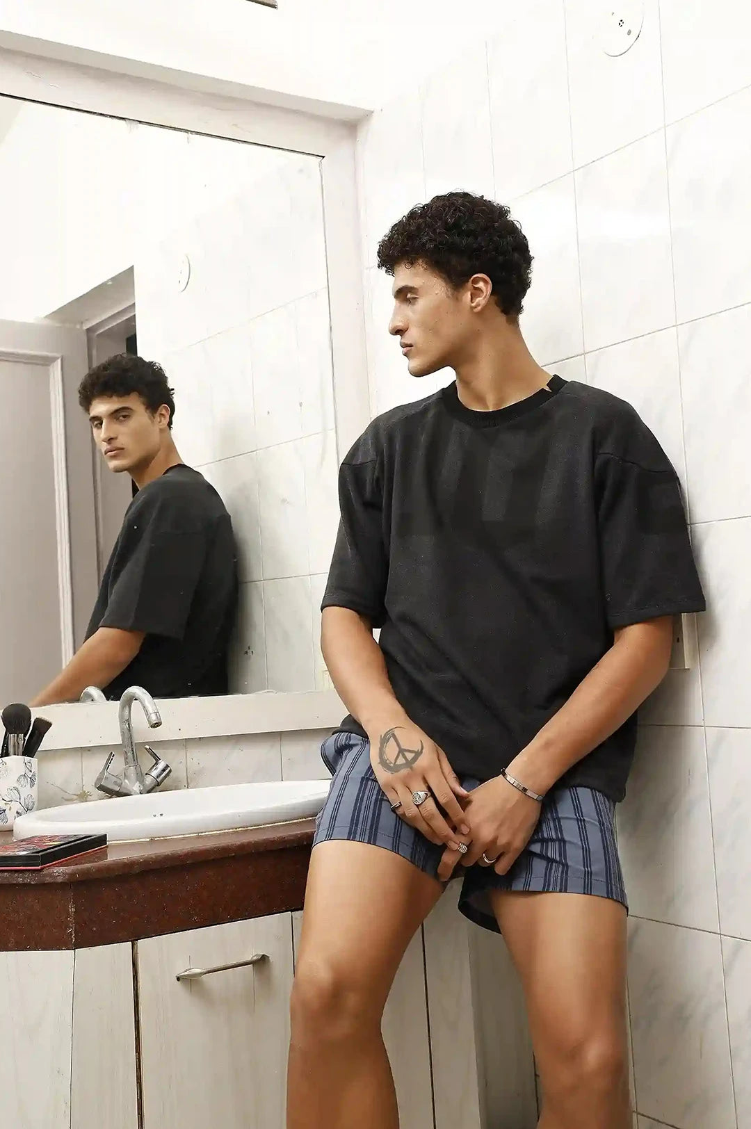 Person wearing a black t-shirt and plaid shorts standing in a bathroom.