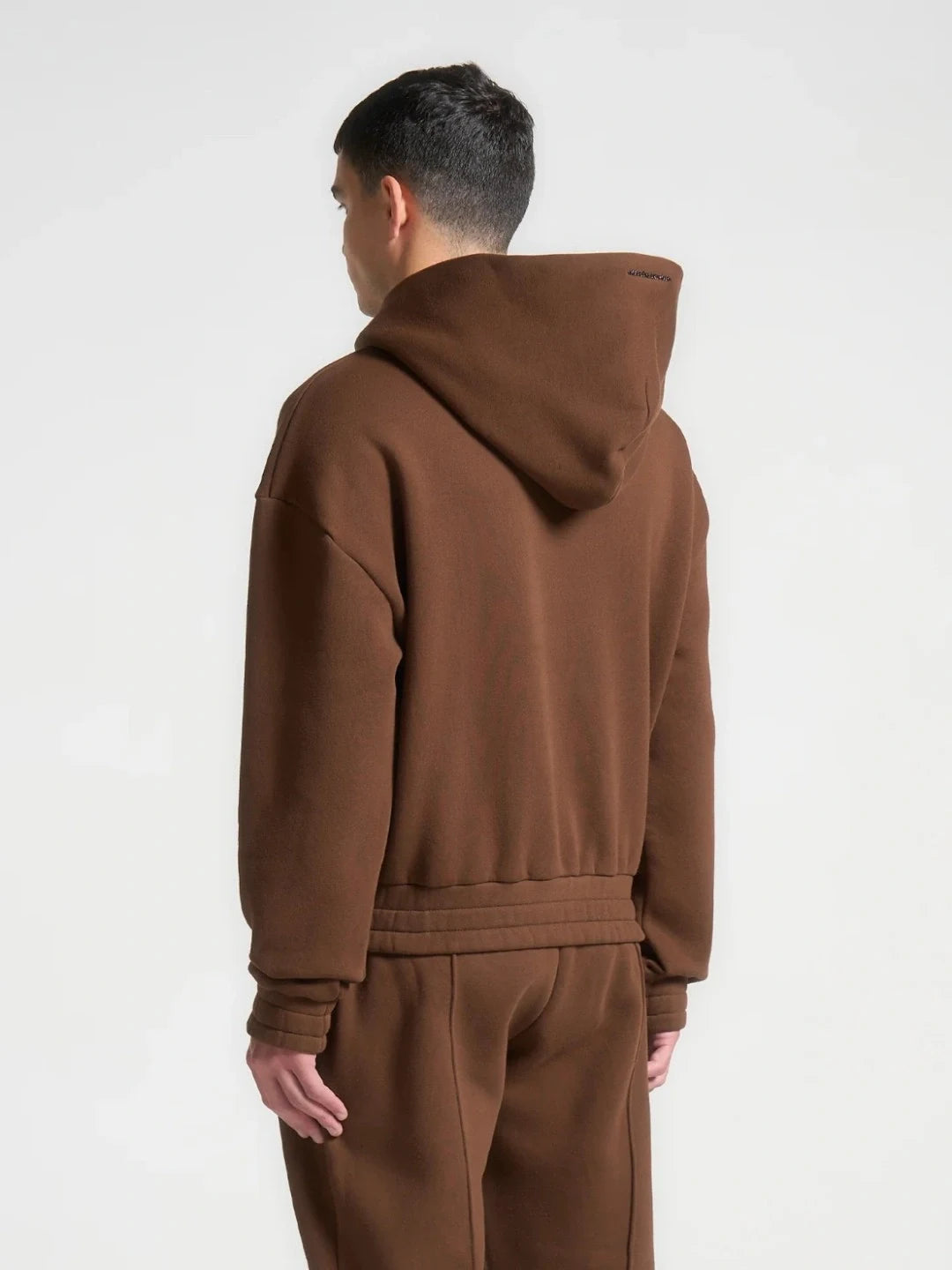 Person wearing a brown hoodie and pants on a white background