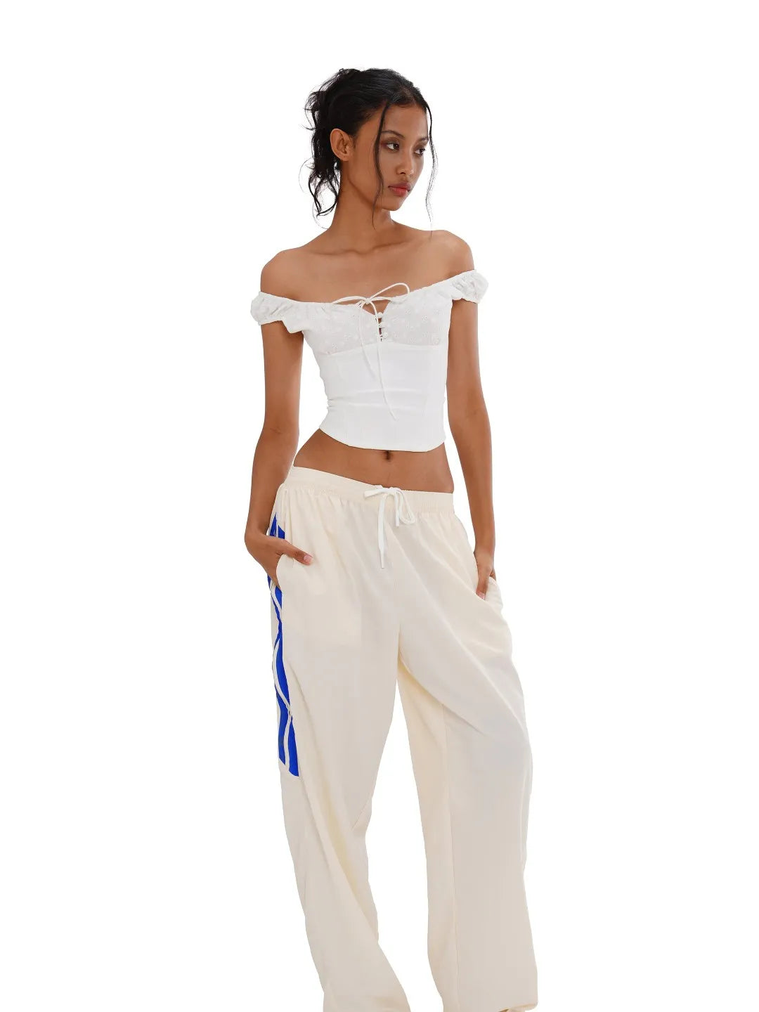 Woman wearing a white off-shoulder top and cream pants with a blue stripe on a white background