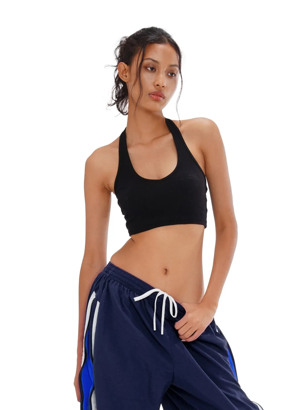 Woman wearing a black sports bra and navy blue pants with white drawstrings on a white background
