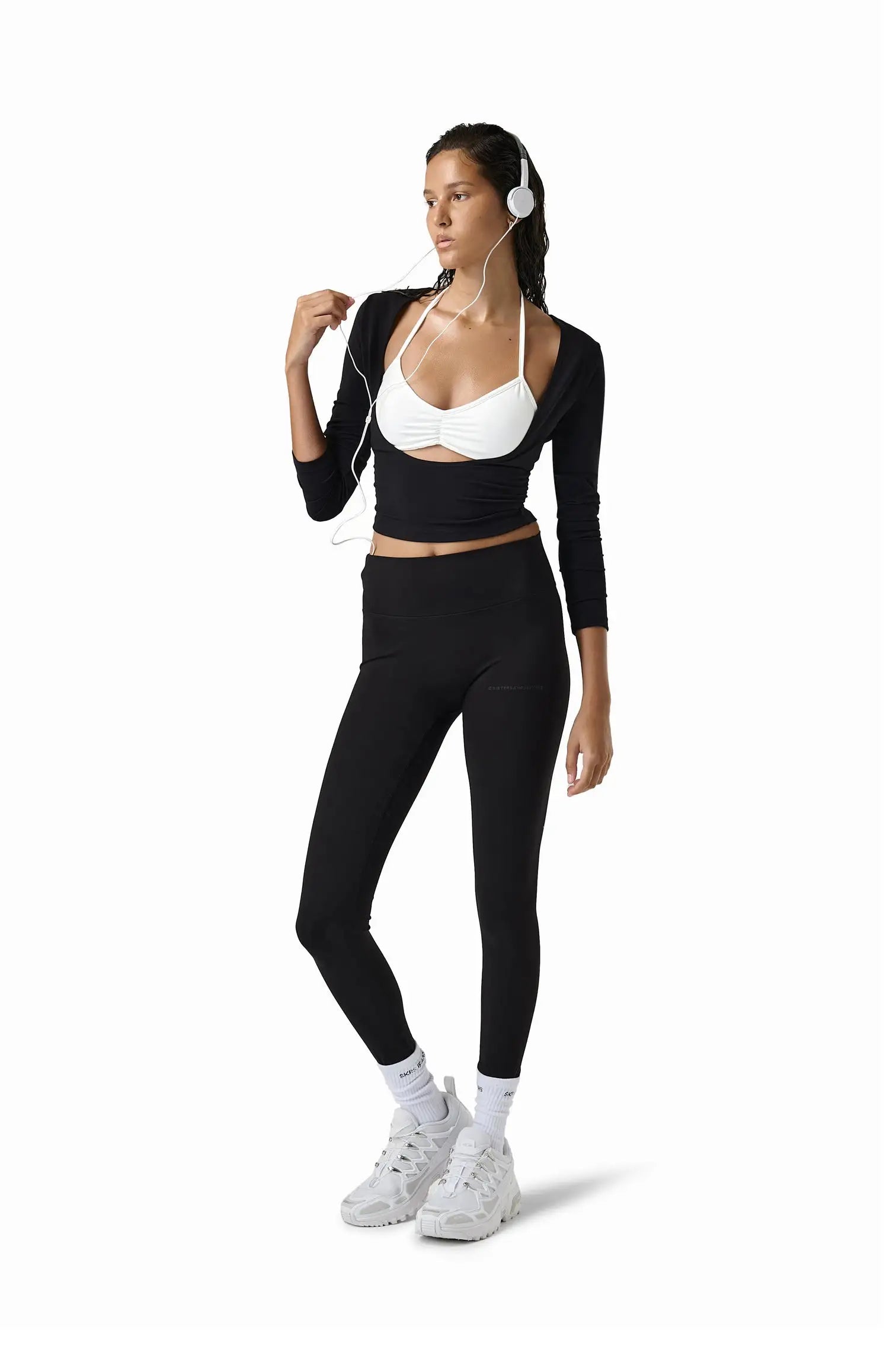 Woman in black athletic outfit with white sports bra and headphones on a white background