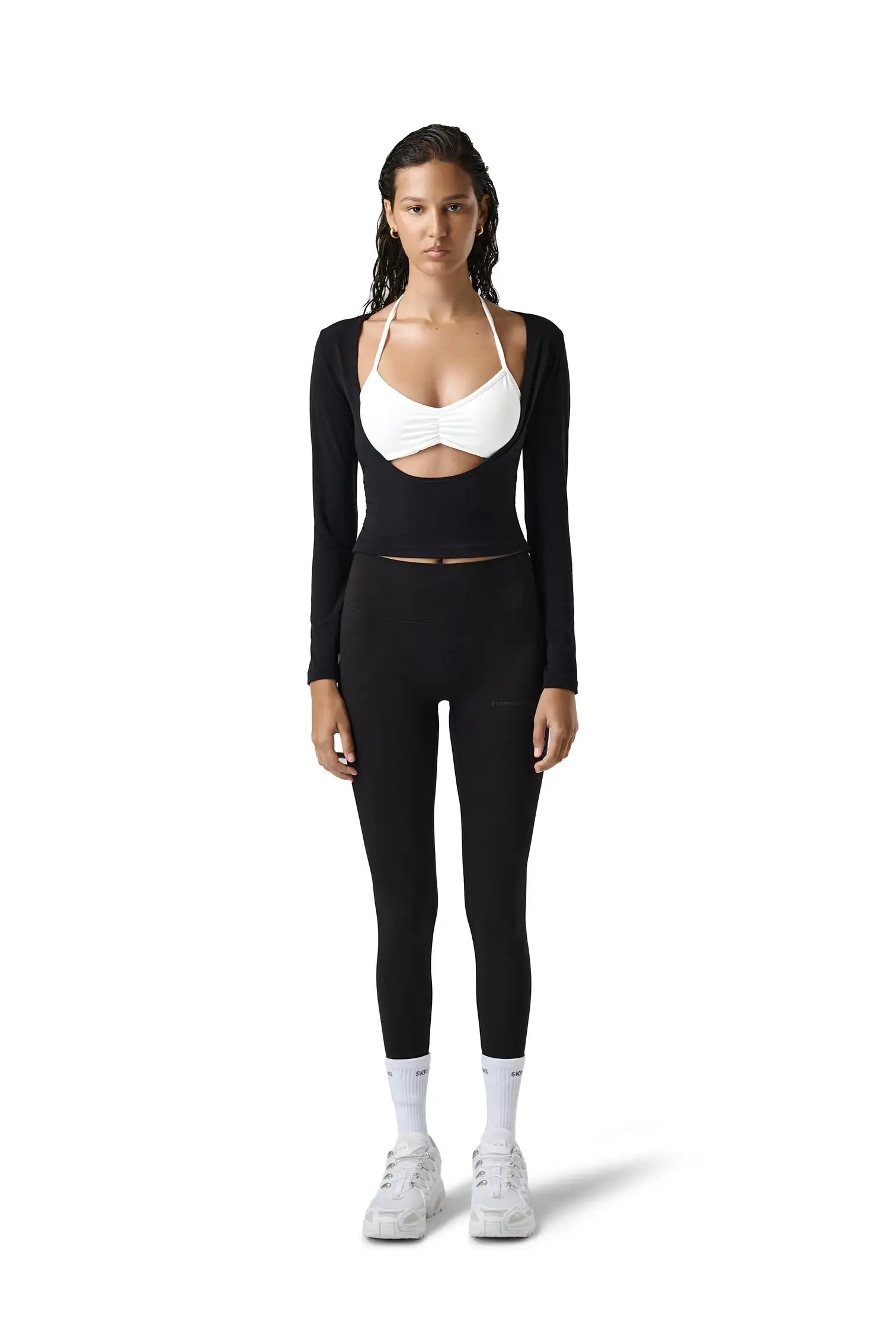 Woman wearing a black long-sleeve crop top and leggings with a white sports bra on a white background