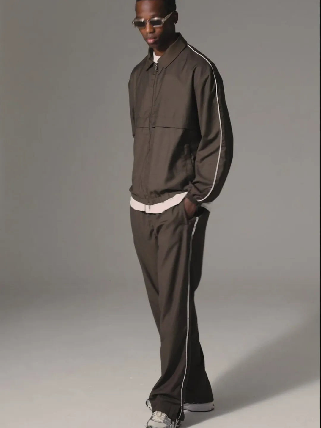 Man wearing a brown tracksuit with white stripes on a gray background