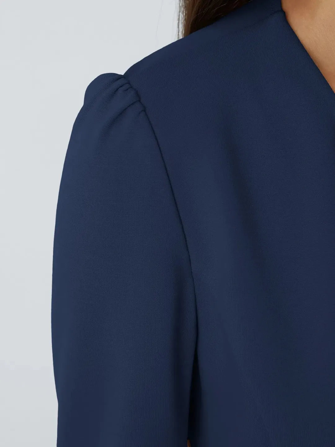 Woman wearing a blue buisness jacket with gold buttons on a light gray background