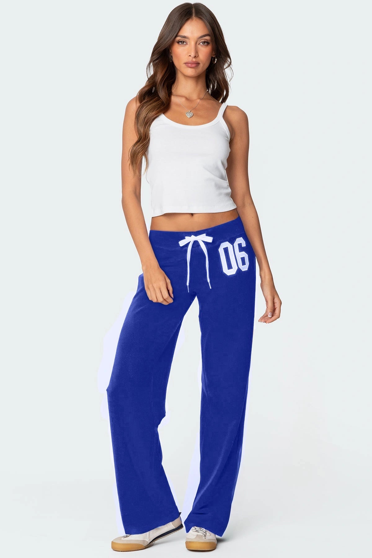 Woman wearing blue sweatpants with a white drawstring and '06' printed on them, paired with a white tank top.