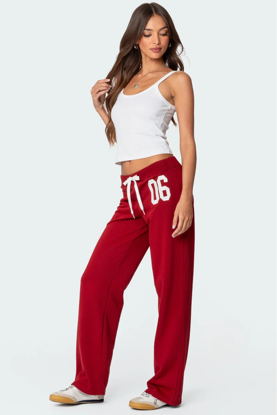 Woman wearing a white tank top and red pants with '06' print on a white background