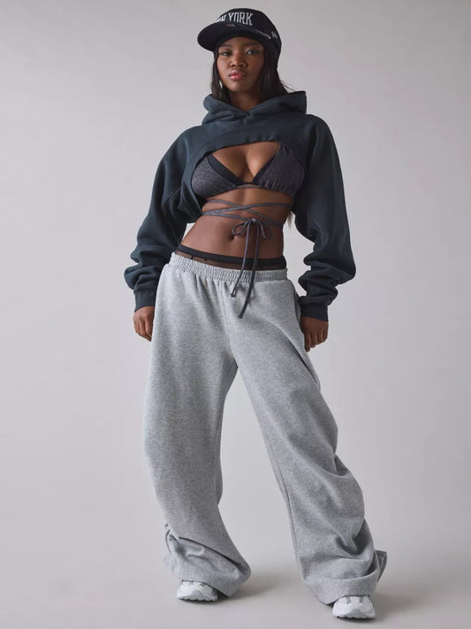 Person wearing a black cropped hoodie with cut-out design over a sports bra and shorts on a plain background