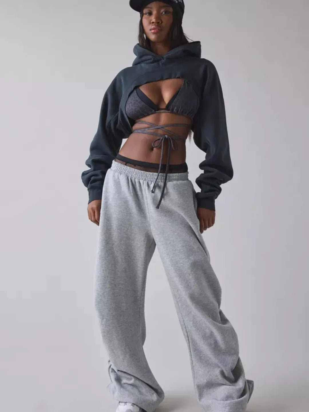 Person wearing a black cropped hoodie with cut-out design over a sports bra and shorts on a plain background