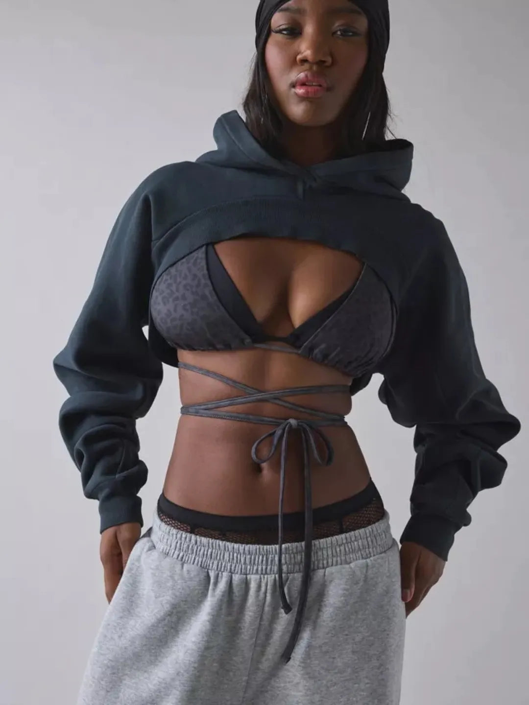 Person wearing a black cropped hoodie with cut-out design over a sports bra and shorts on a plain background