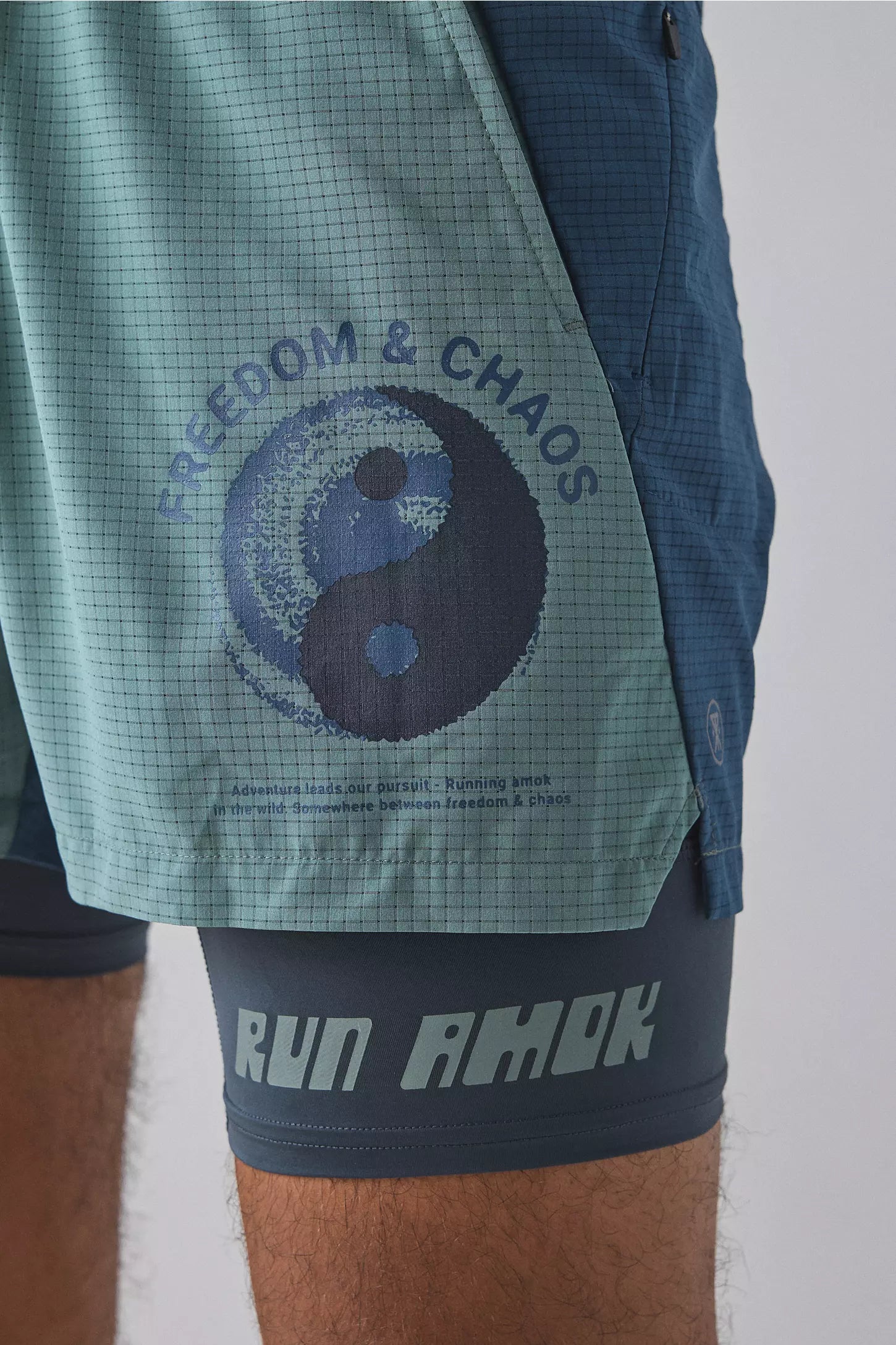 Green shorts with a yin yang symbol and 'Freedom & Chaos' text, worn by a person.