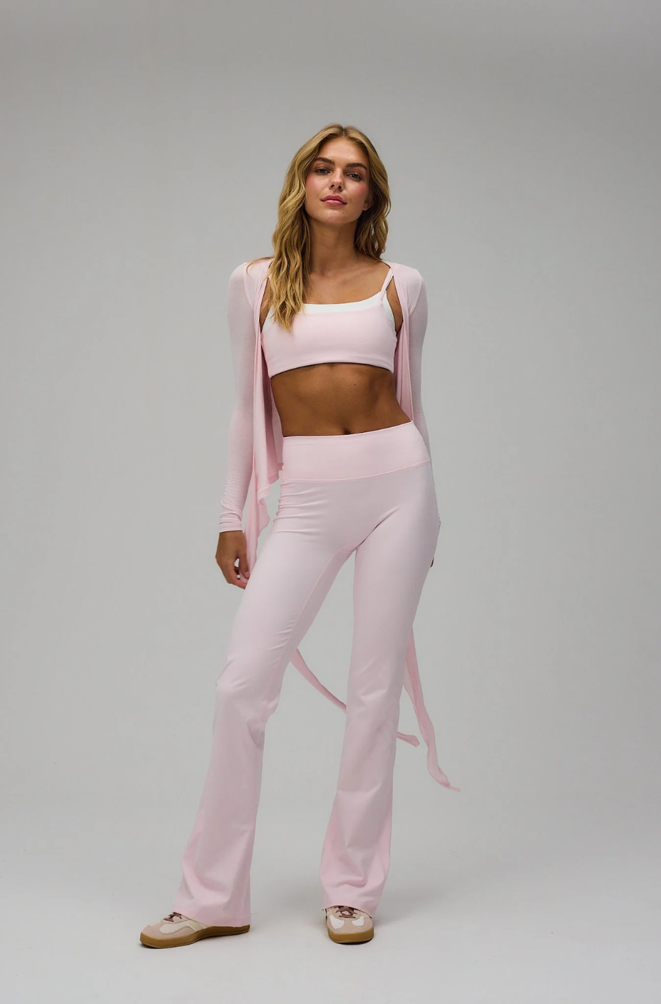 Woman wearing a pink outfit with a cardigan on a gray background