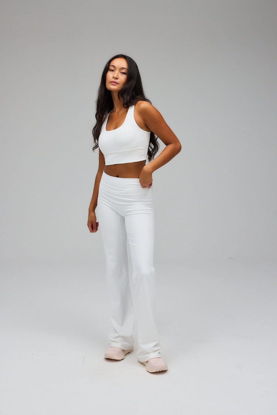 Woman wearing a white sports bra and pants on a gray background
