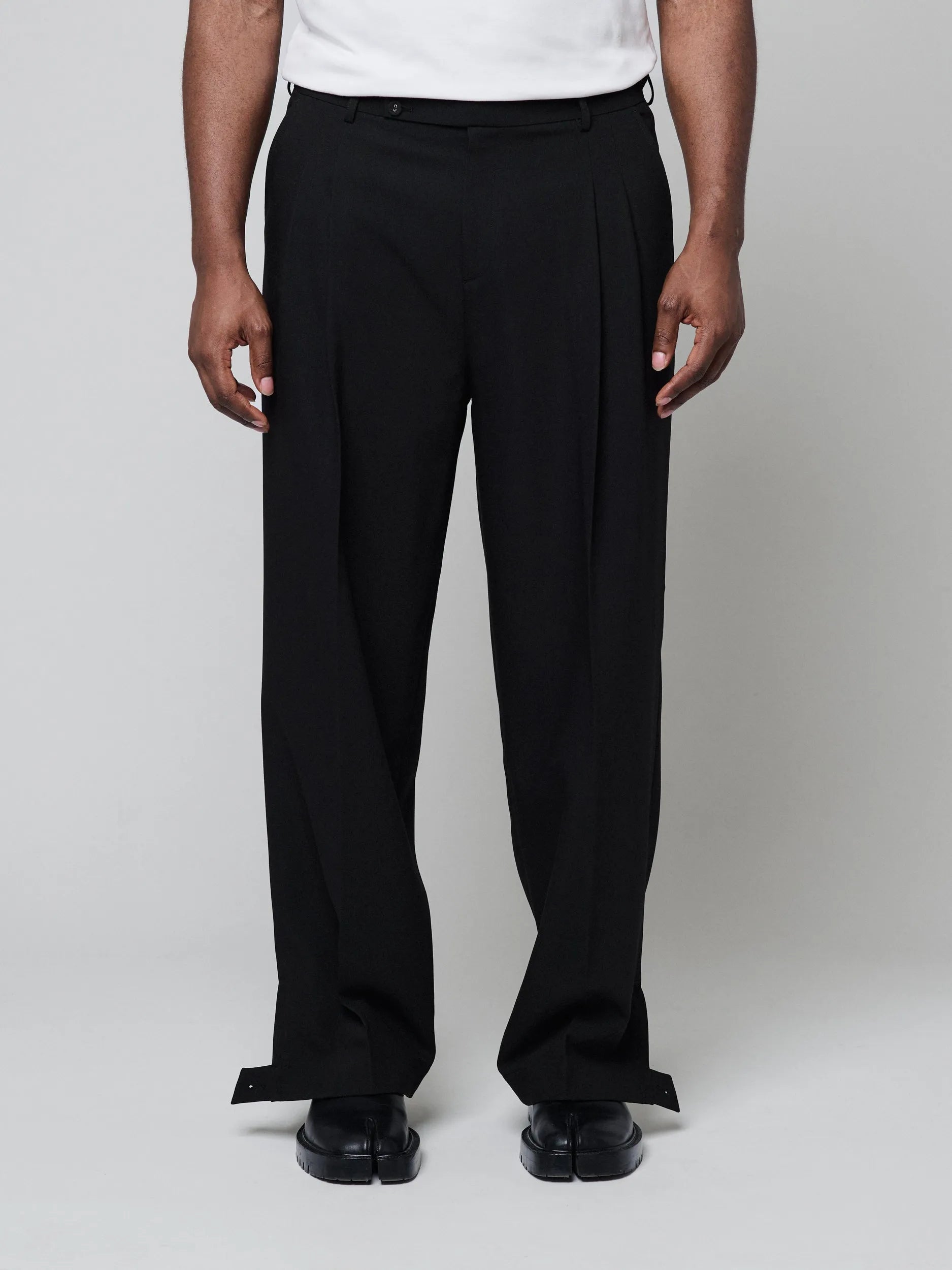 Black Pants with Double front pleats and adjustable side tabs offer a comfortable, customizable fit, while functional pockets and zip-open hem slits add versatility. Crafted from a smooth cotton blend, they are ideal for refined casual, elevated streetwear, and polished off-duty styling.