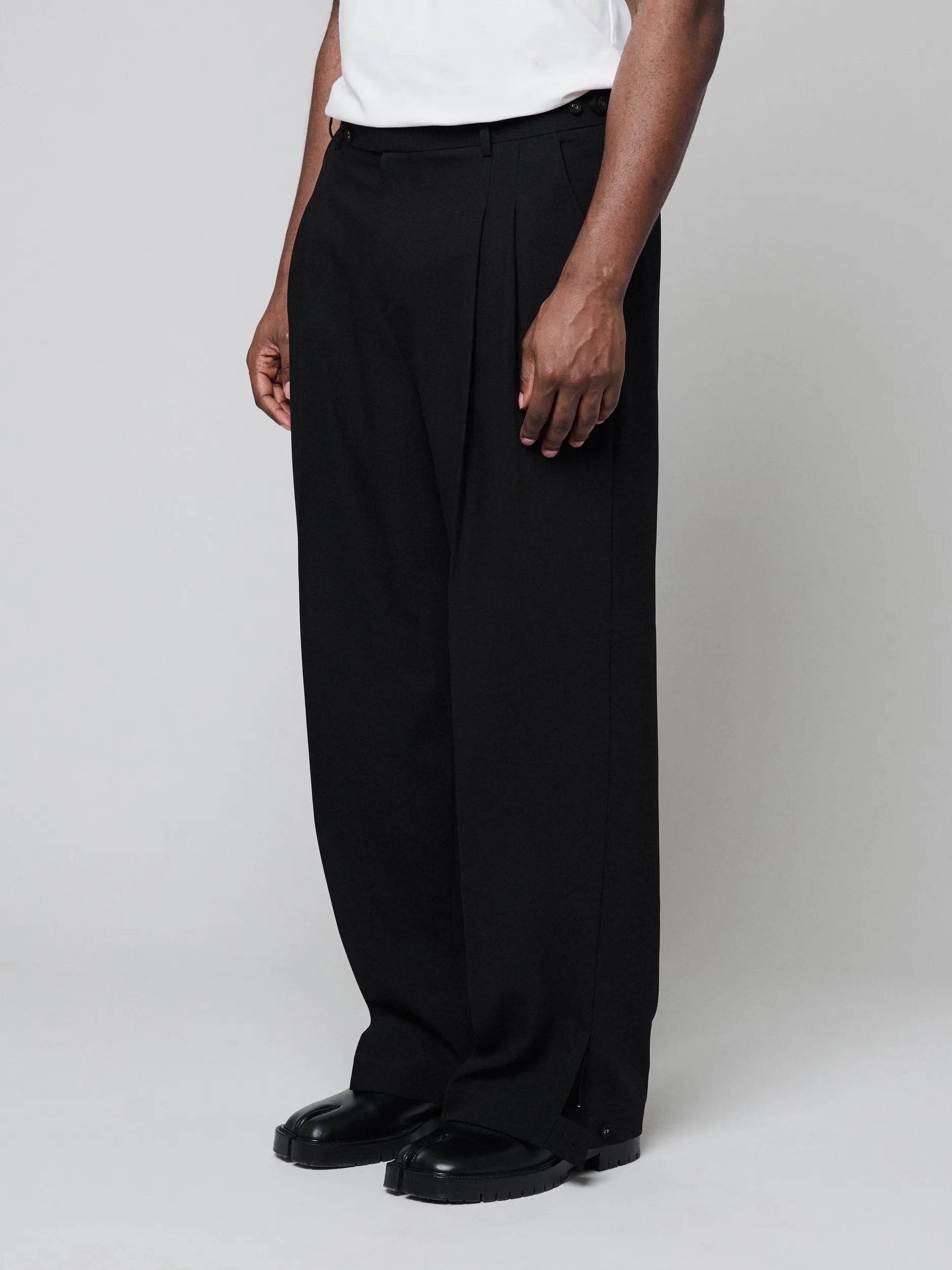 Black Pants with Double front pleats and adjustable side tabs offer a comfortable, customizable fit, while functional pockets and zip-open hem slits add versatility. Crafted from a smooth cotton blend, they are ideal for refined casual, elevated streetwear, and polished off-duty styling.