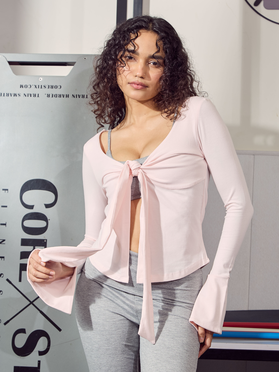 Woman wearing a light pink cardigan over a grey top and pants in an indoor setting.