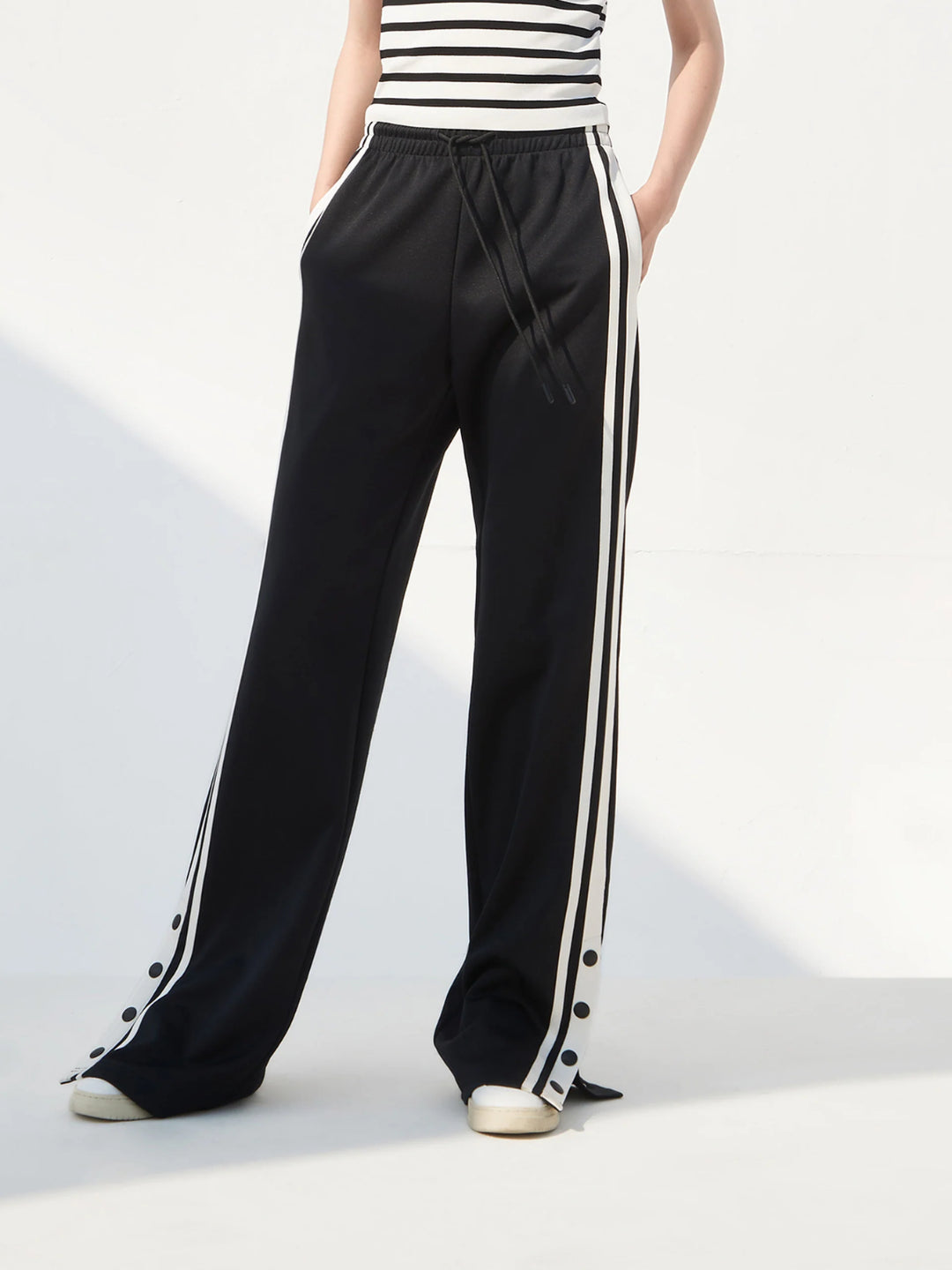 black slit snap button tracks pants with an elastic drawstring waist, featuring white stripes on the legs and a side slit on one leg
