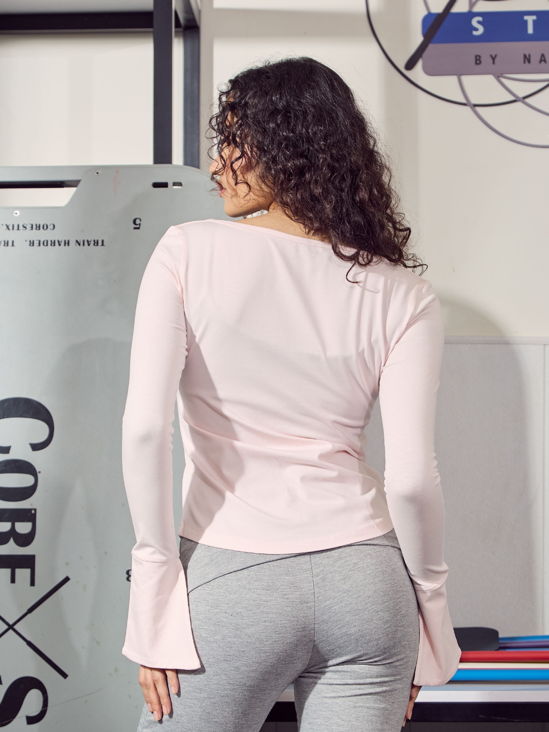 Person wearing a light pink long-sleeve top and grey leggings in an indoor setting.