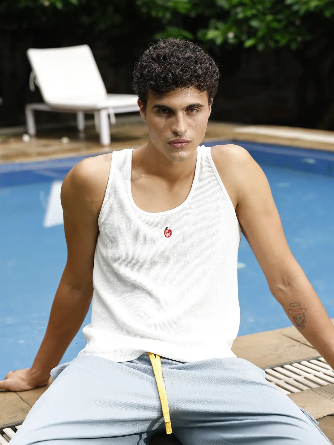 Man sitting by a pool wearing a white tank top with a red logo