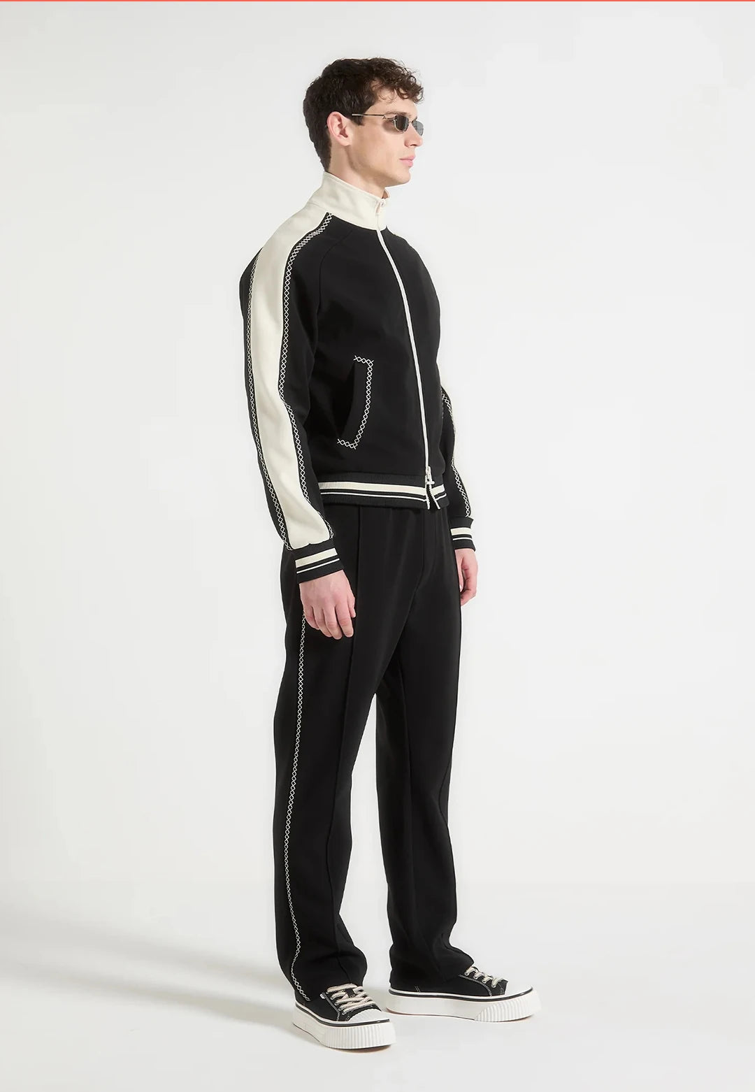 Person wearing a black and white tracksuit with sunglasses on a white background