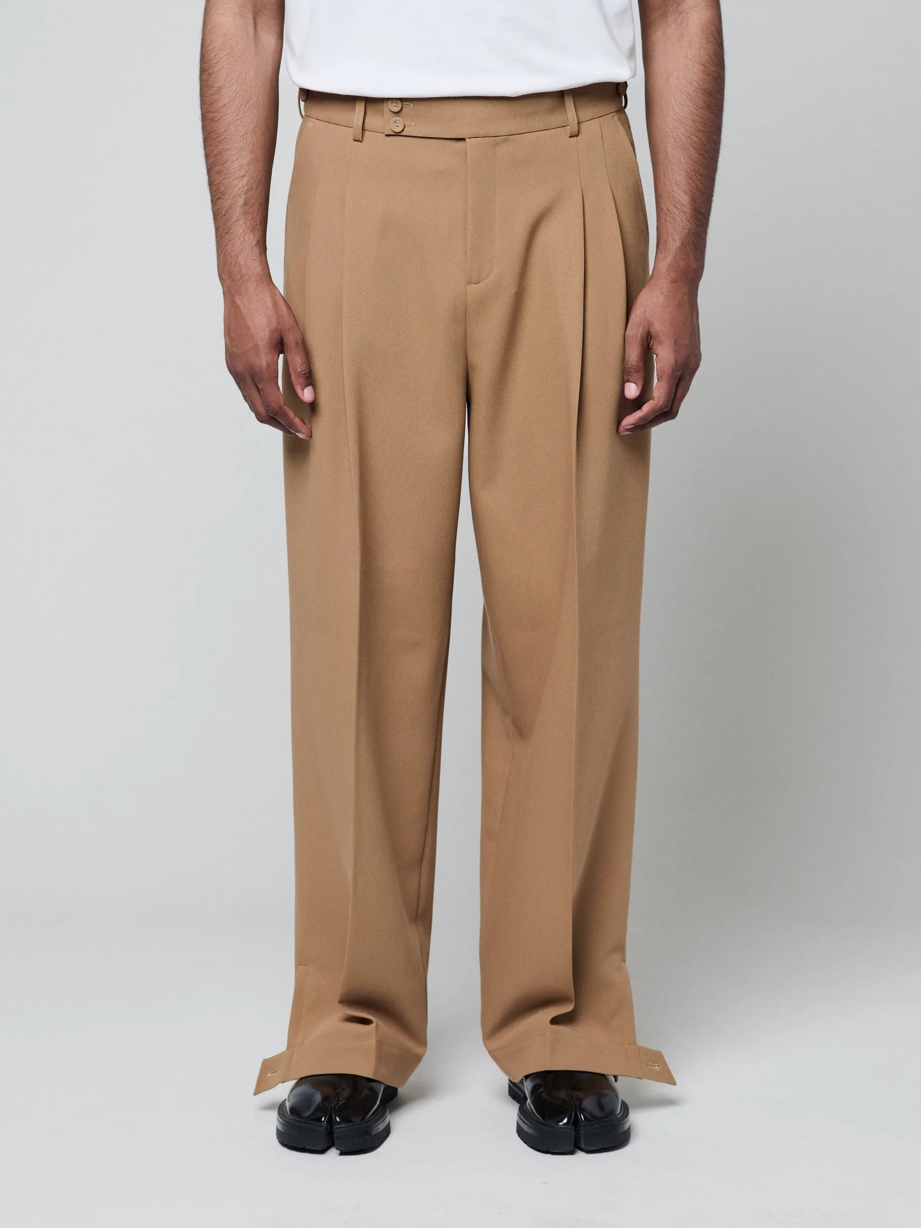 Tan Pants with Double front pleats and adjustable side tabs offer a comfortable, customizable fit, while functional pockets and zip-open hem slits add versatility. Crafted from a smooth cotton blend, they are ideal for refined casual, elevated streetwear, and polished off-duty styling.