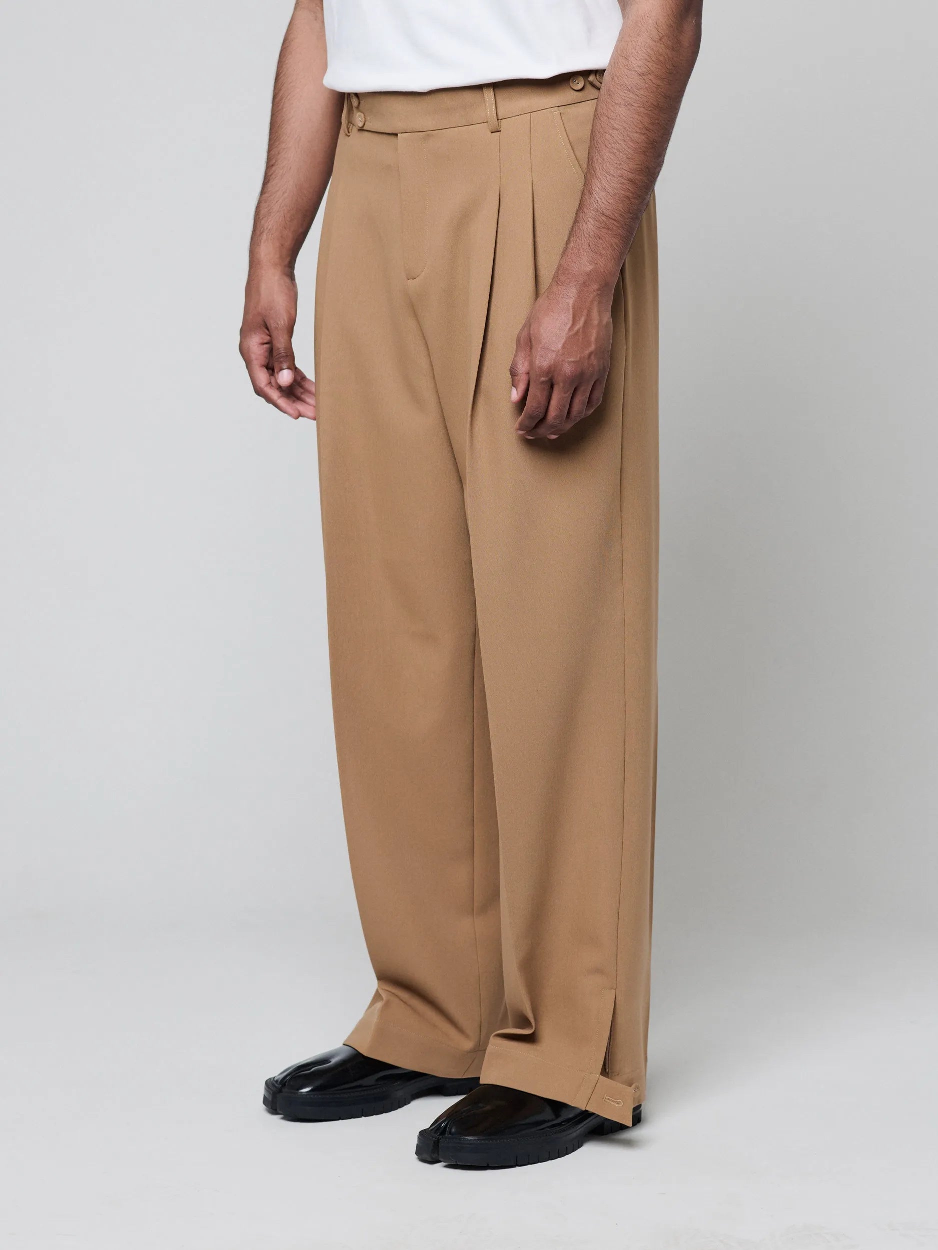 Tan Pants with Double front pleats and adjustable side tabs offer a comfortable, customizable fit, while functional pockets and zip-open hem slits add versatility. Crafted from a smooth cotton blend, they are ideal for refined casual, elevated streetwear, and polished off-duty styling.
