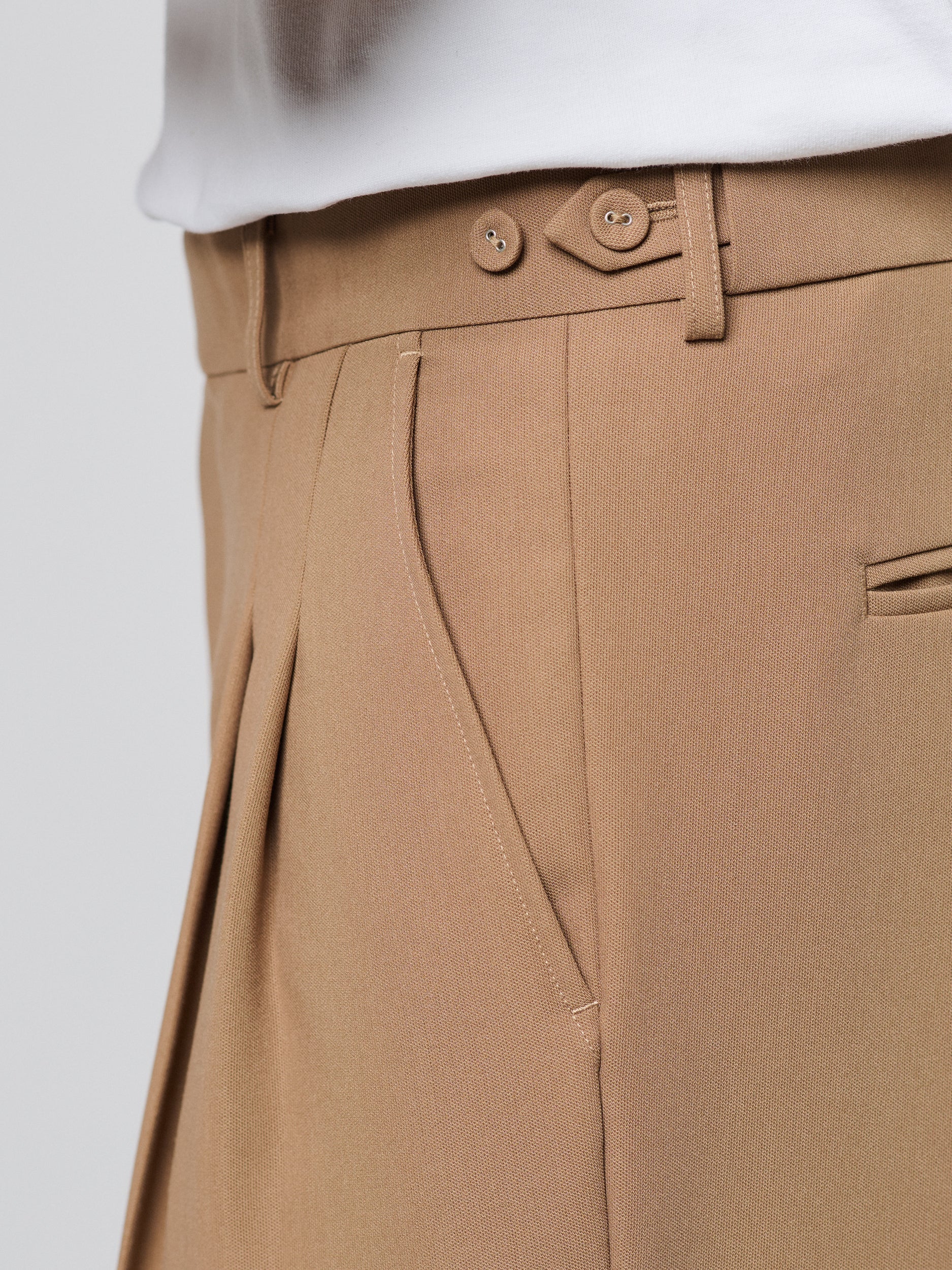 Tan Pants with Double front pleats and adjustable side tabs offer a comfortable, customizable fit, while functional pockets and zip-open hem slits add versatility. Crafted from a smooth cotton blend, they are ideal for refined casual, elevated streetwear, and polished off-duty styling.