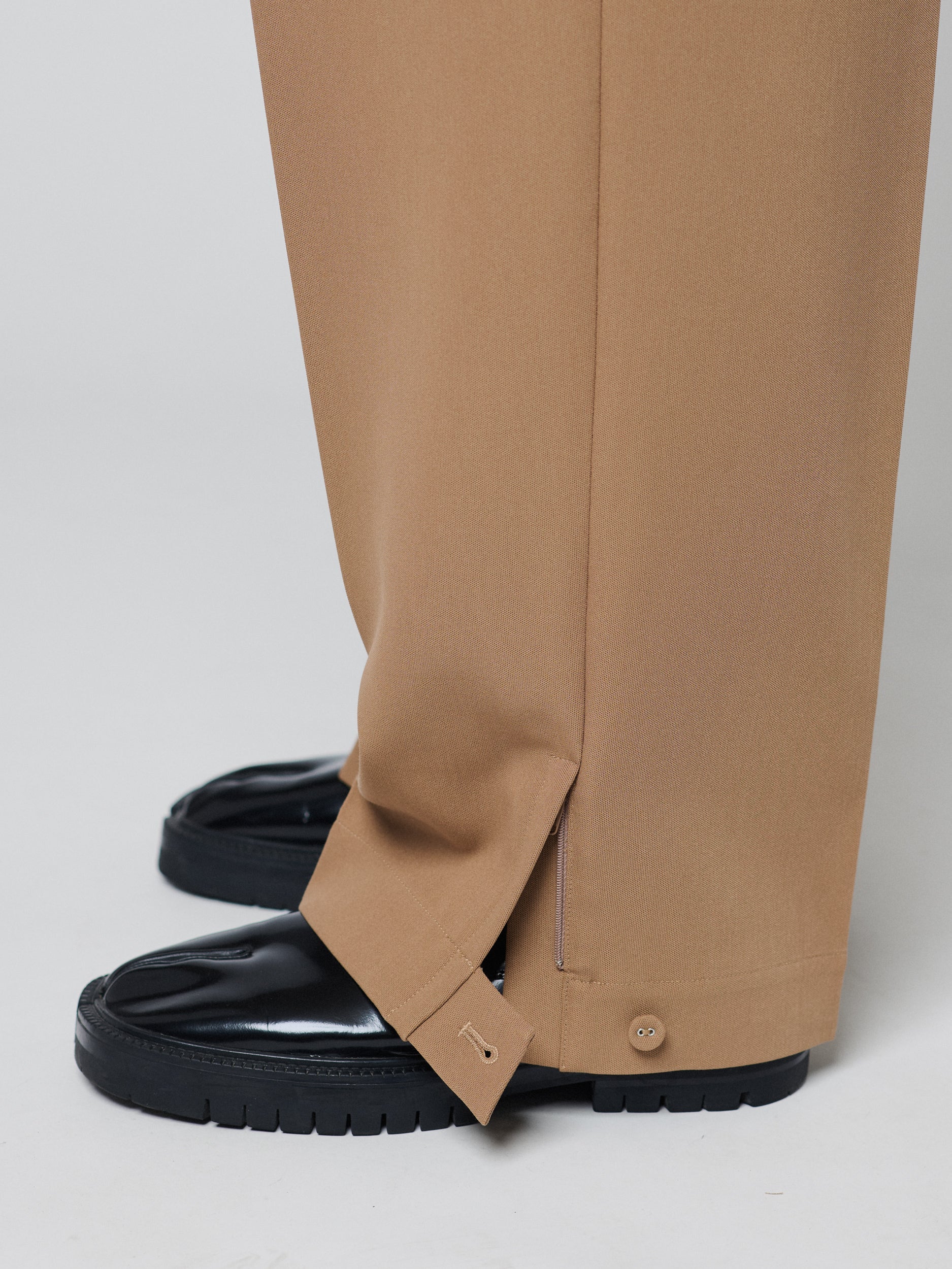 Tan Pants with Double front pleats and adjustable side tabs offer a comfortable, customizable fit, while functional pockets and zip-open hem slits add versatility. Crafted from a smooth cotton blend, they are ideal for refined casual, elevated streetwear, and polished off-duty styling.