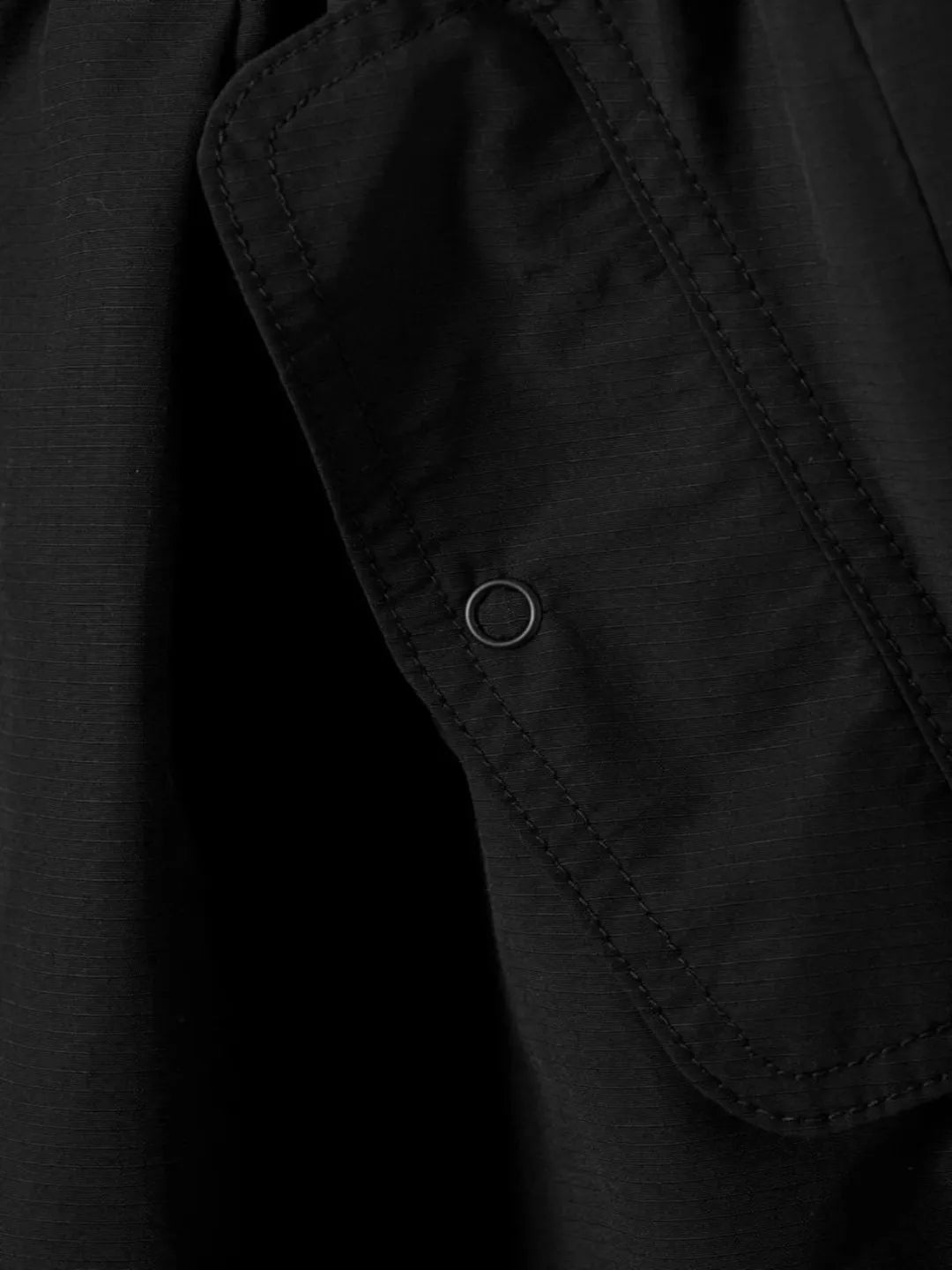 Close-up of a black jacket with a button detail on a dark background