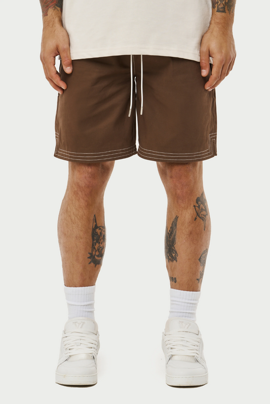 This image displays a model wearing a pair of contrast stitch woven shorts, perfect for a relaxed yet stylish look. The shorts are brown with a distinctive white contrast stitching that accentuates the seams and pockets, adding a modern touch to the classic design.