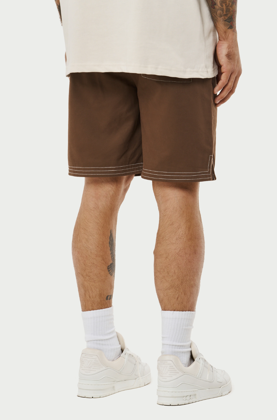Model wearing a pair of contrast stitch woven shorts, perfect for a relaxed yet stylish look. The shorts are brown with a distinctive white contrast stitching that accentuates the seams and pockets, adding a modern touch to the classic design.
