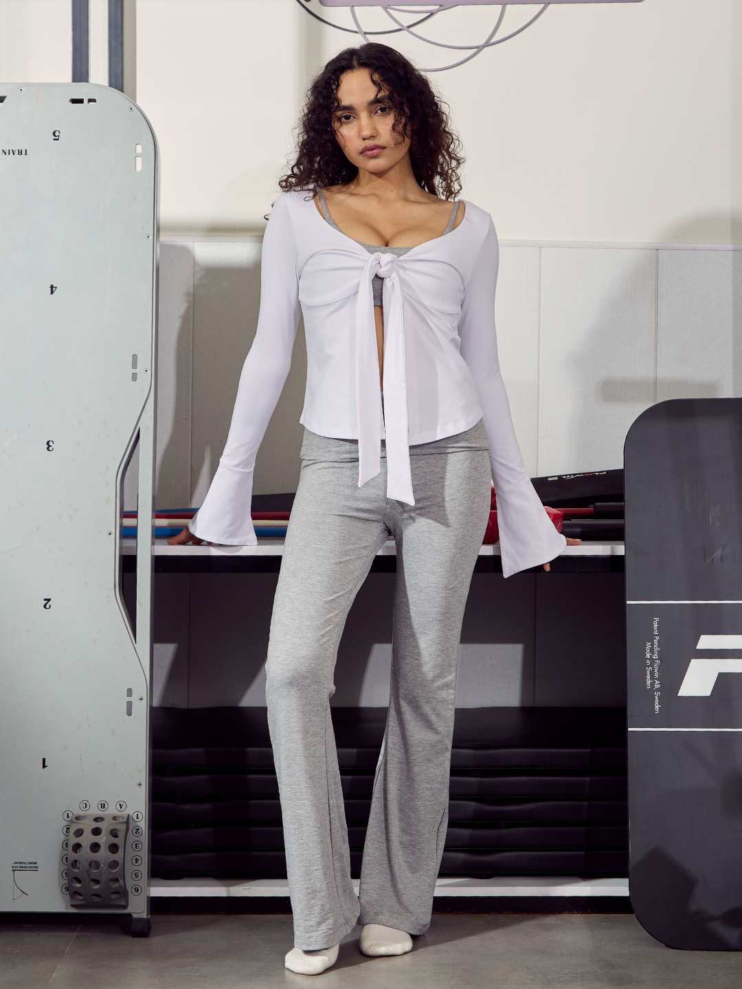 Woman in a white top and grey pants standing in a futuristic setting with machinery.