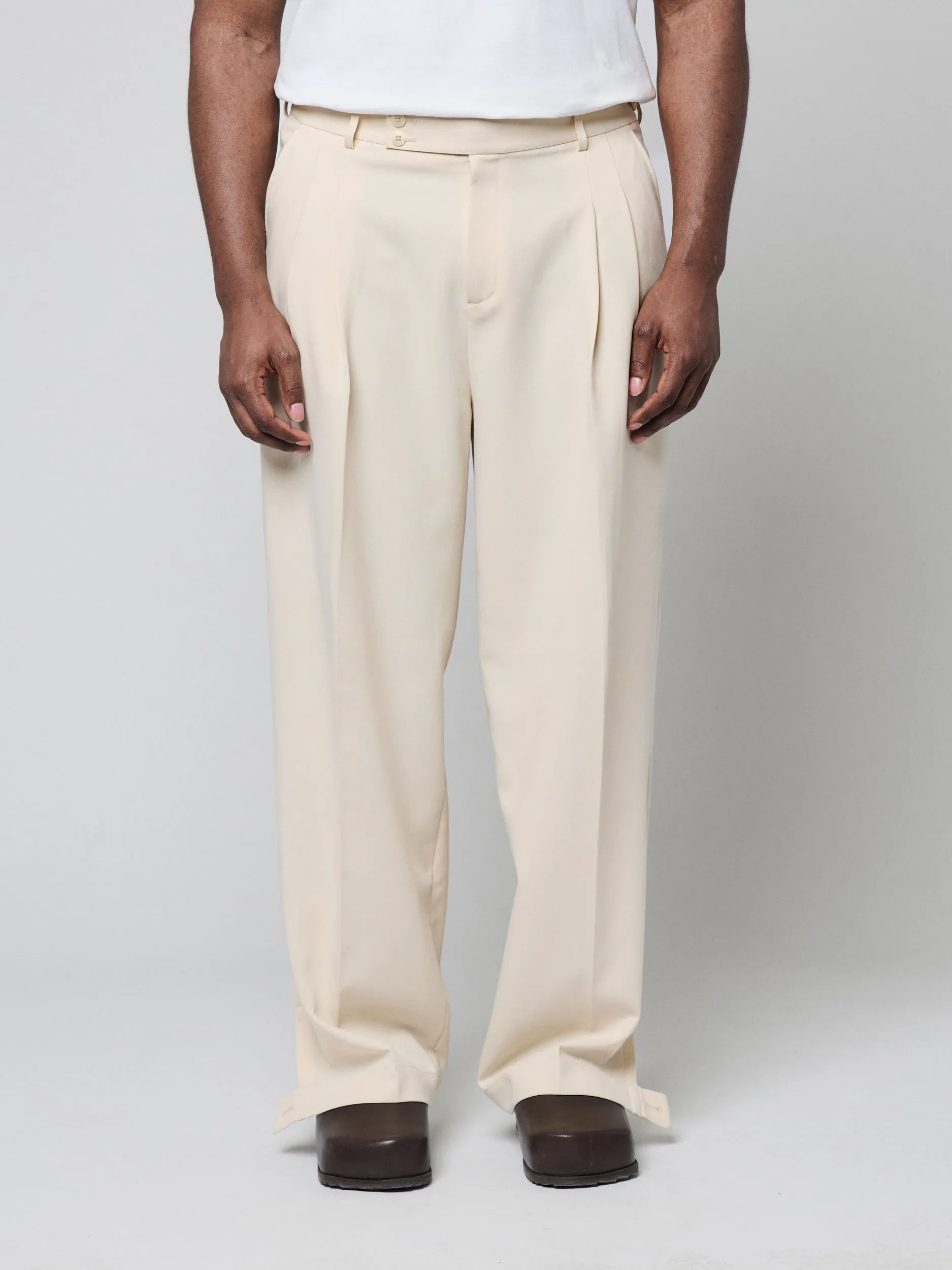 Beige Pants with Double front pleats and adjustable side tabs offer a comfortable, customizable fit, while functional pockets and zip-open hem slits add versatility. Crafted from a smooth cotton blend, they are ideal for refined casual, elevated streetwear, and polished off-duty styling.