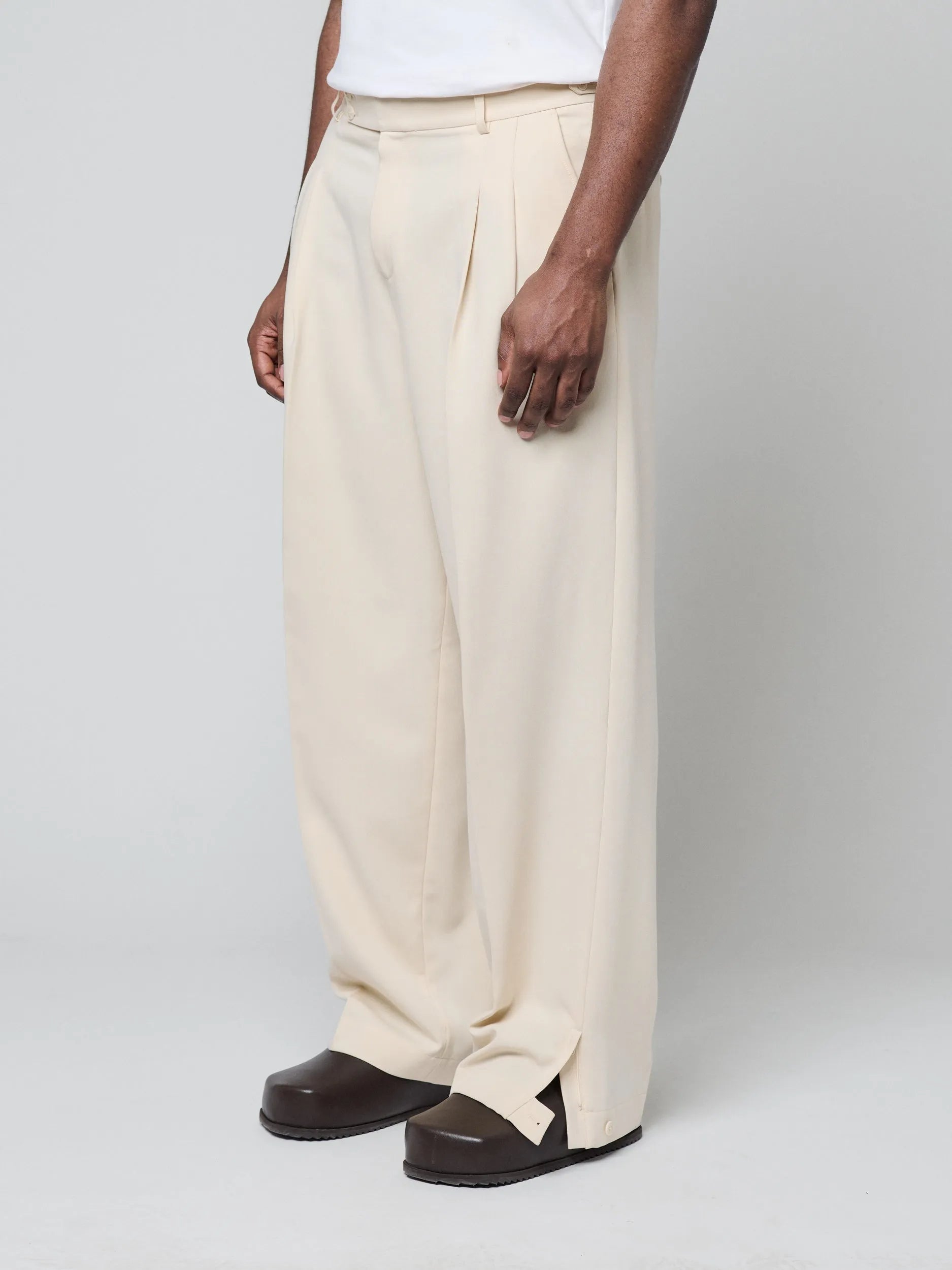 Beige Pants with Double front pleats and adjustable side tabs offer a comfortable, customizable fit, while functional pockets and zip-open hem slits add versatility. Crafted from a smooth cotton blend, they are ideal for refined casual, elevated streetwear, and polished off-duty styling.