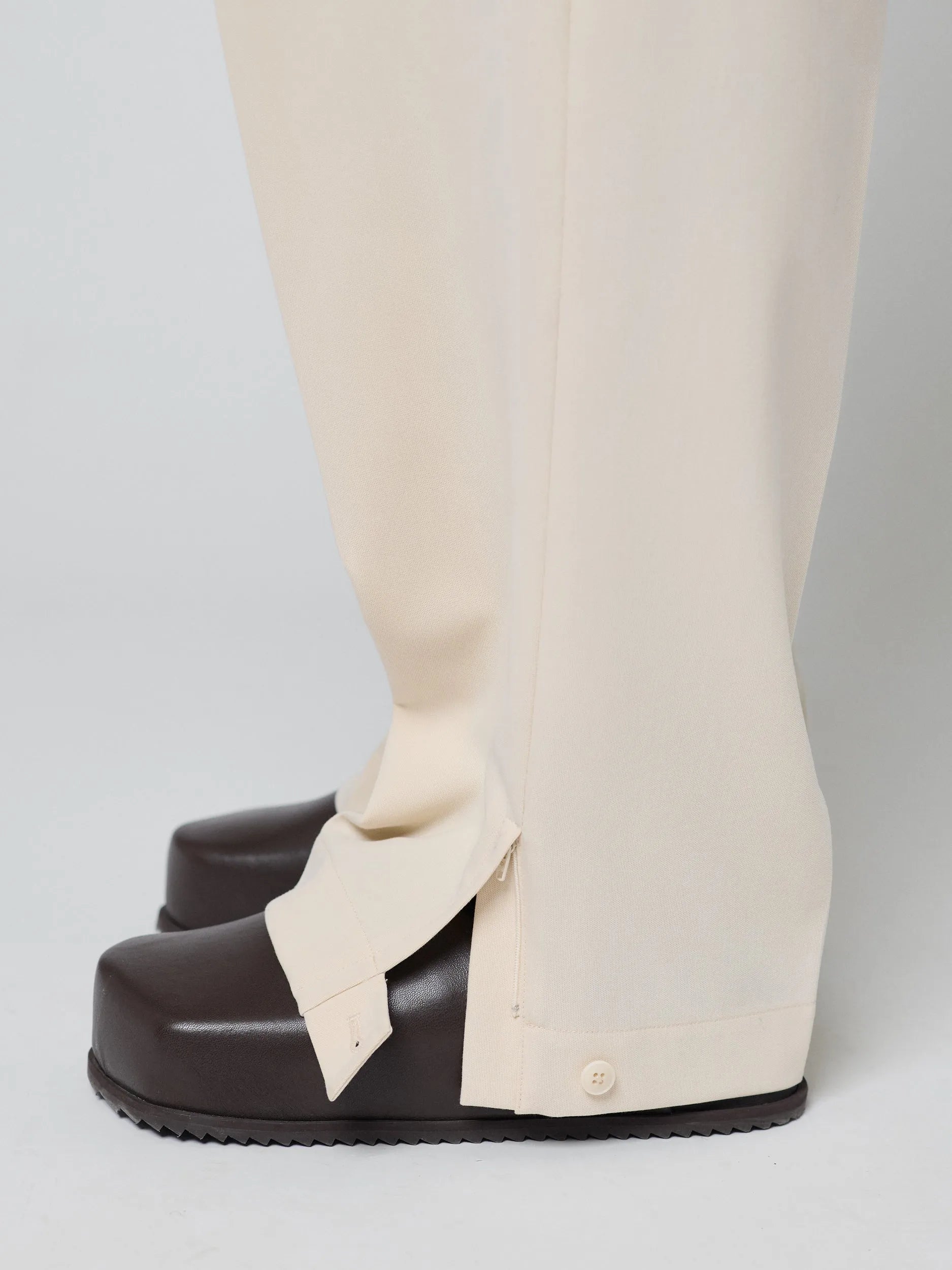 Beige Pants with Double front pleats and adjustable side tabs offer a comfortable, customizable fit, while functional pockets and zip-open hem slits add versatility. Crafted from a smooth cotton blend, they are ideal for refined casual, elevated streetwear, and polished off-duty styling.