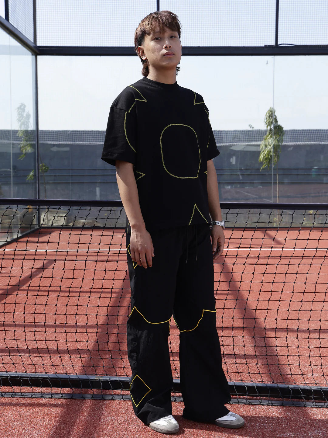 Person wearing a black t-shirt with yellow geometric designs on a tennis court.