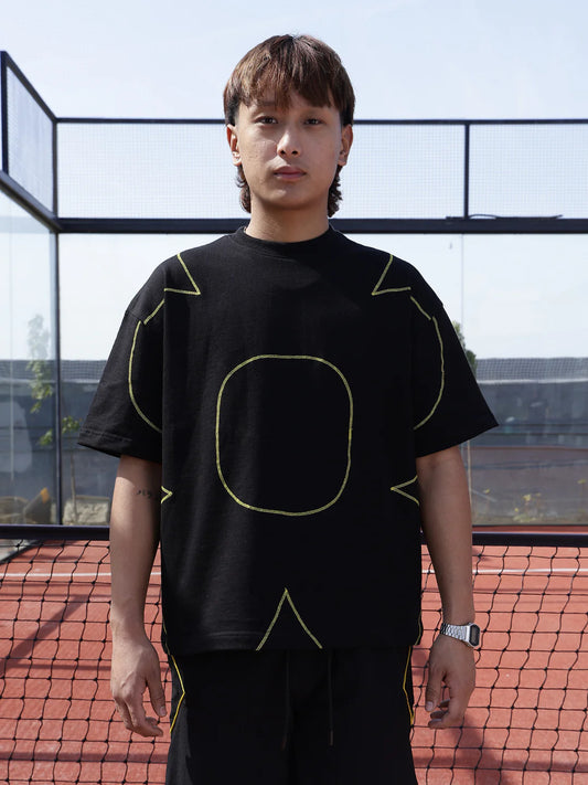 Person wearing a black t-shirt with yellow geometric designs on a tennis court.