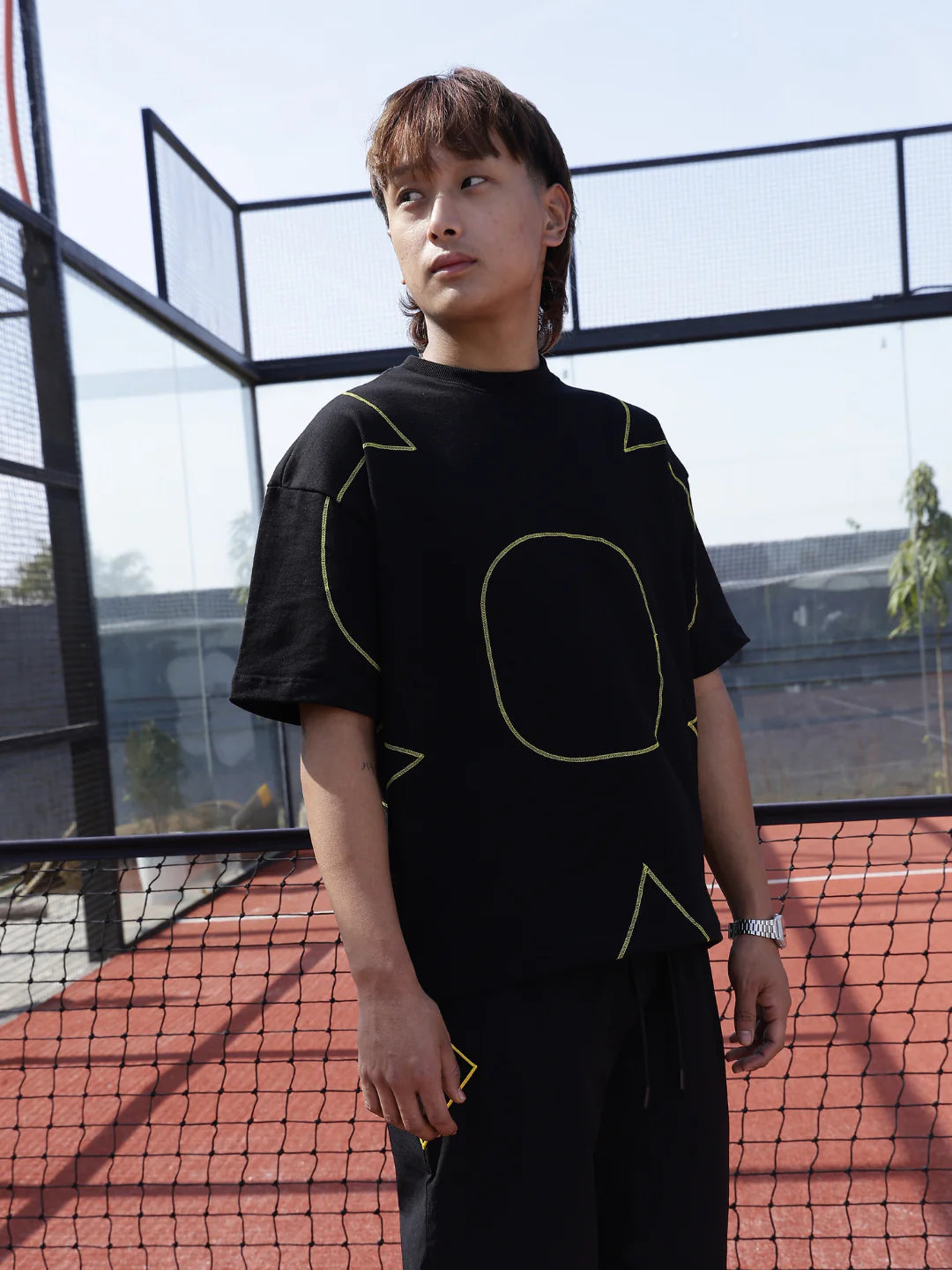 Person wearing a black t-shirt with yellow geometric designs on a tennis court.