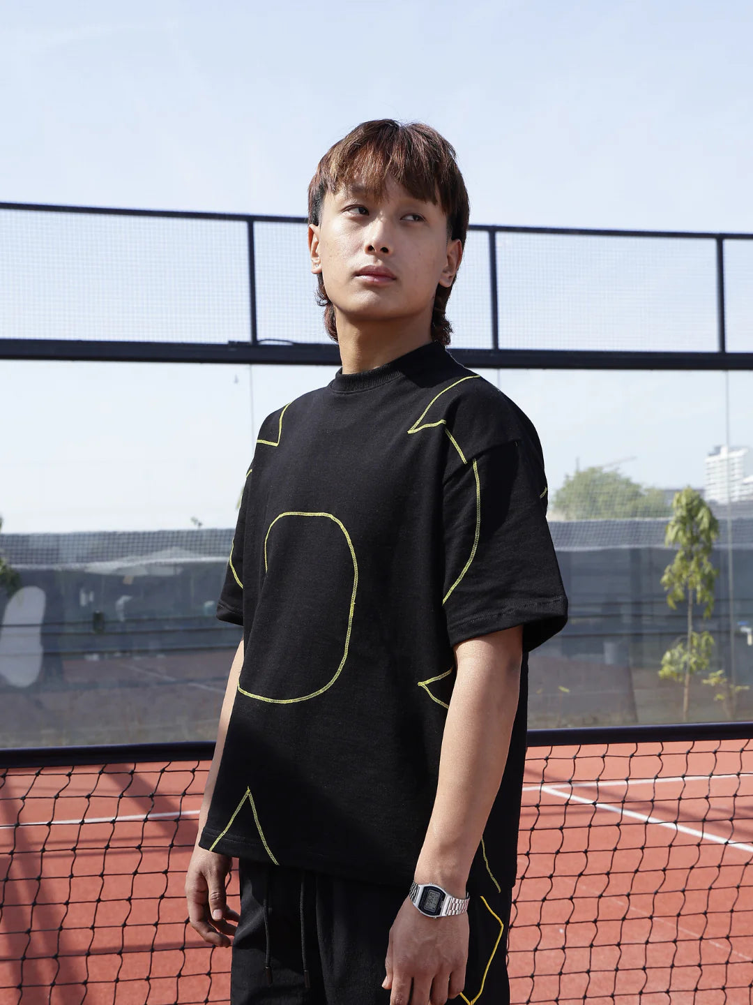 Person wearing a black t-shirt with yellow geometric designs on a tennis court.
