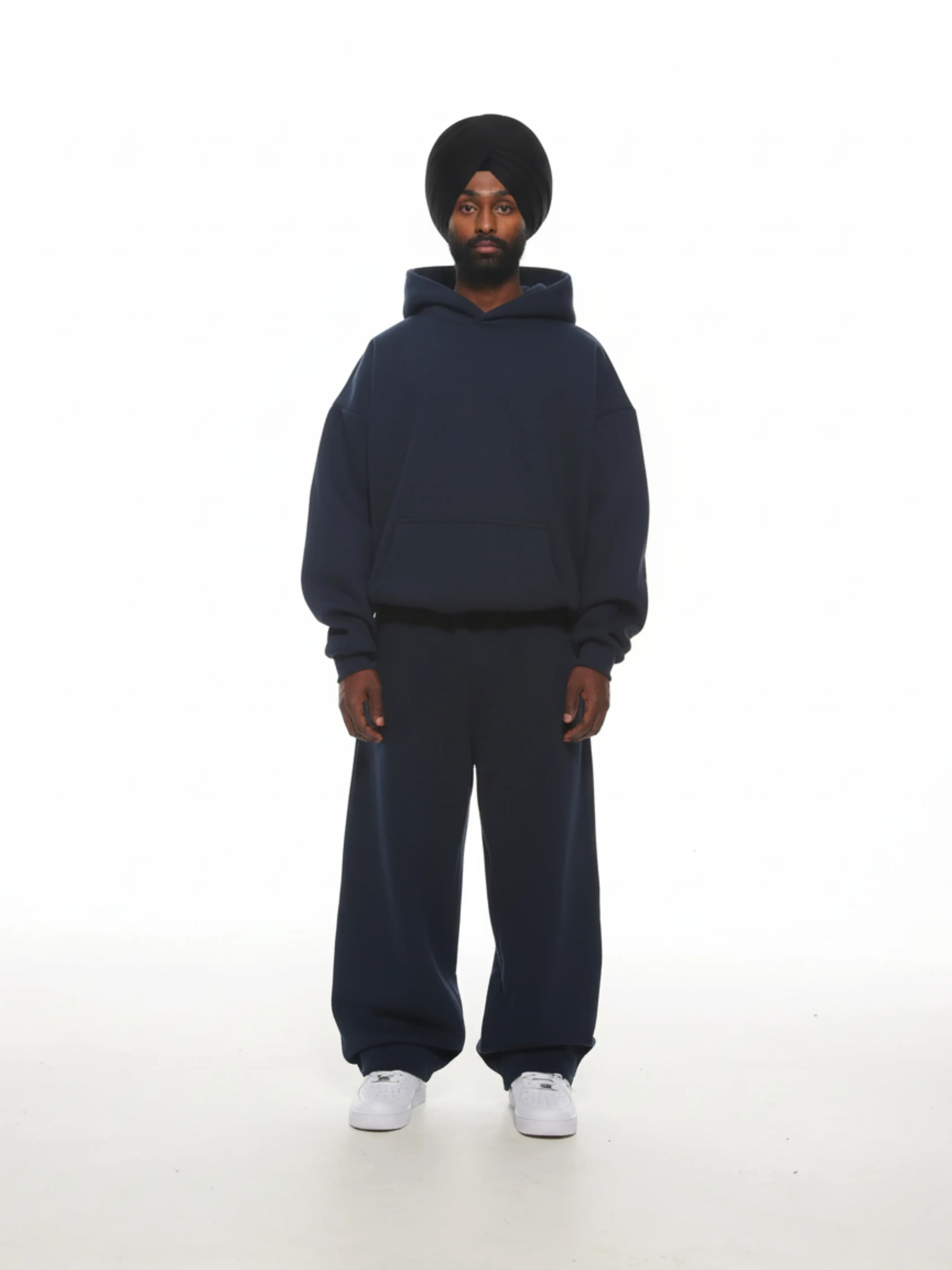 Person wearing a navy blue hoodie and pants set on a white background