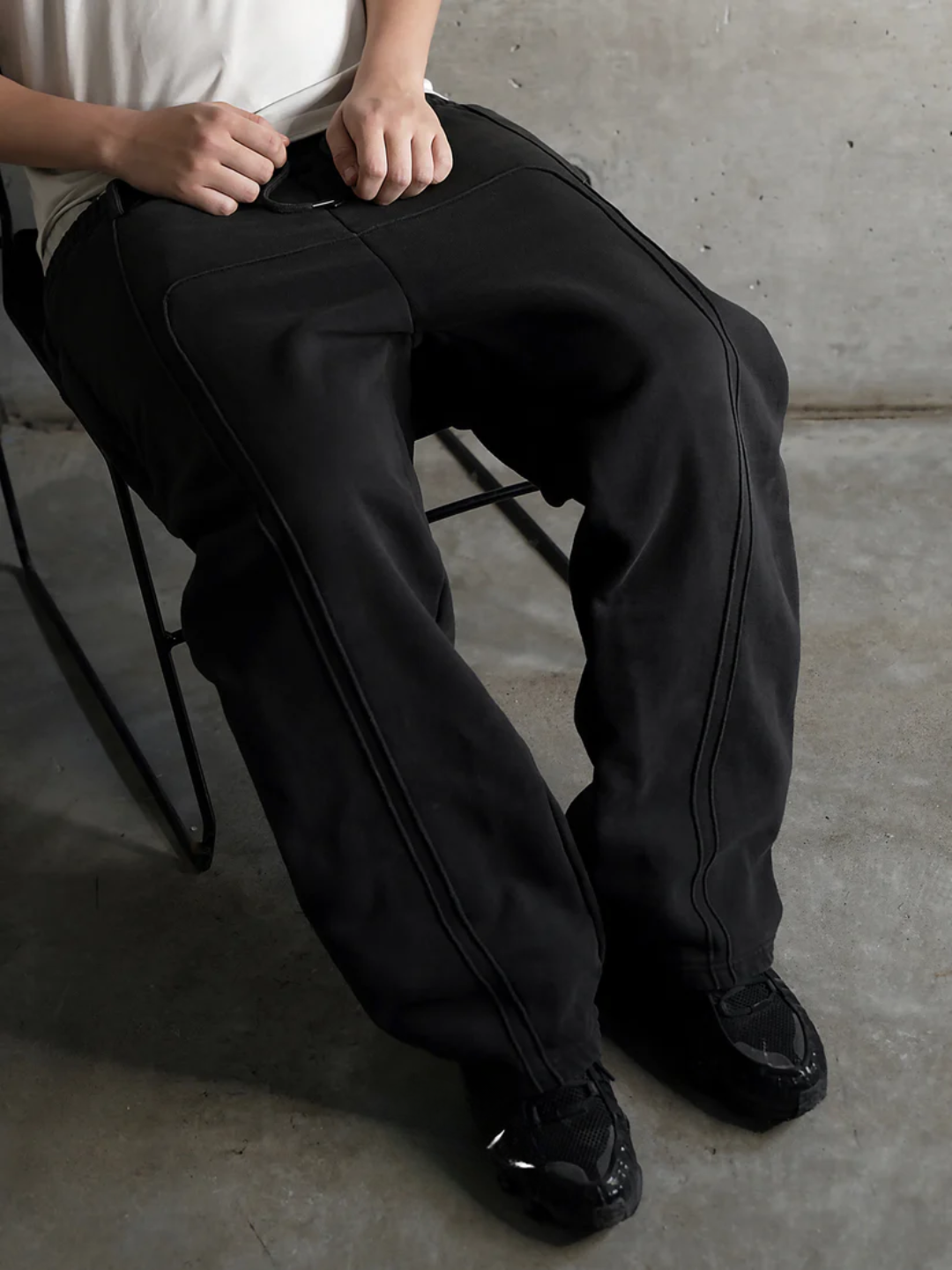 Person wearing black pants sitting on a chair with a concrete floor and wall background