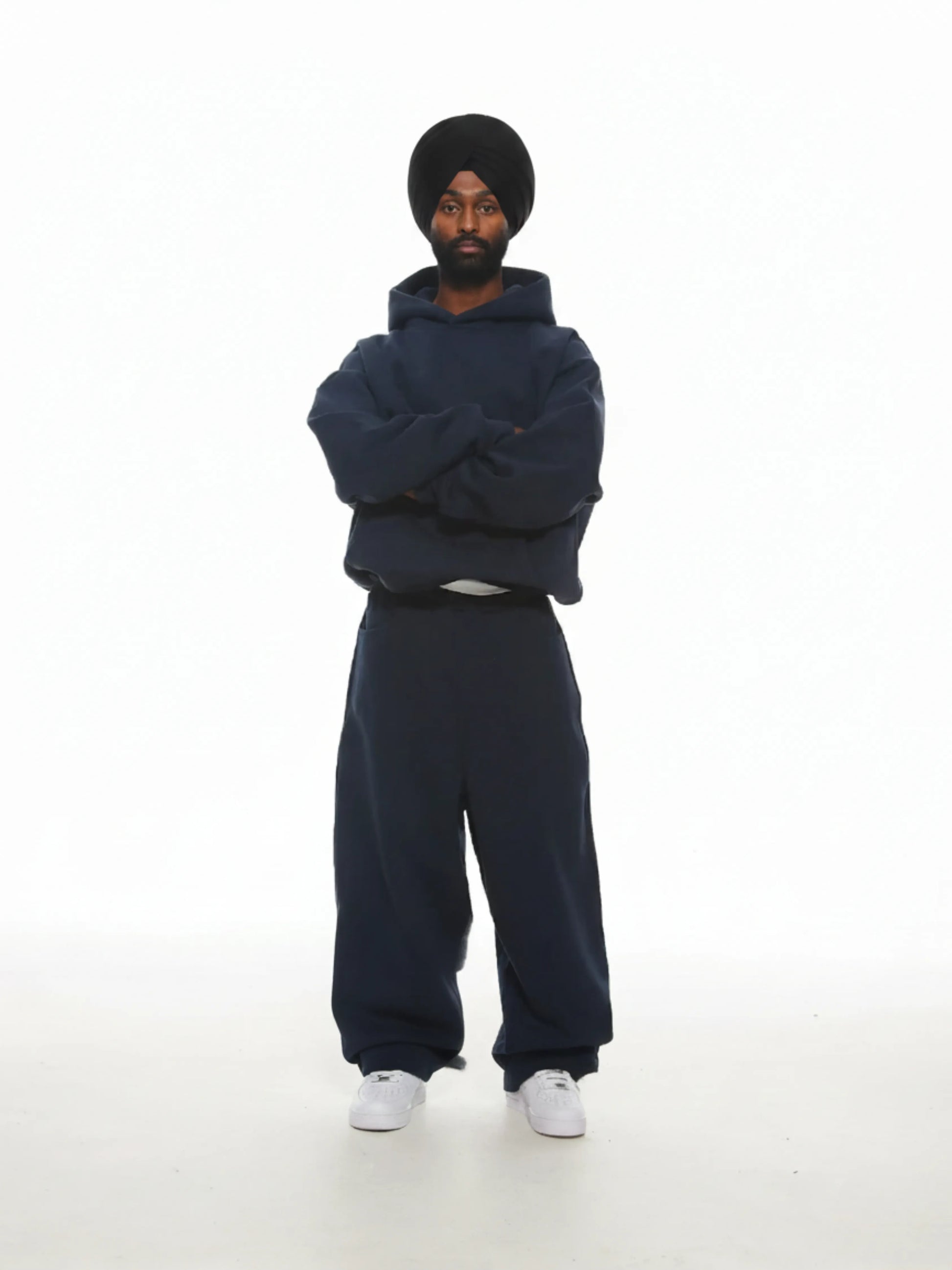 Person wearing a navy blue hoodie and pants with a matching turban on a white background