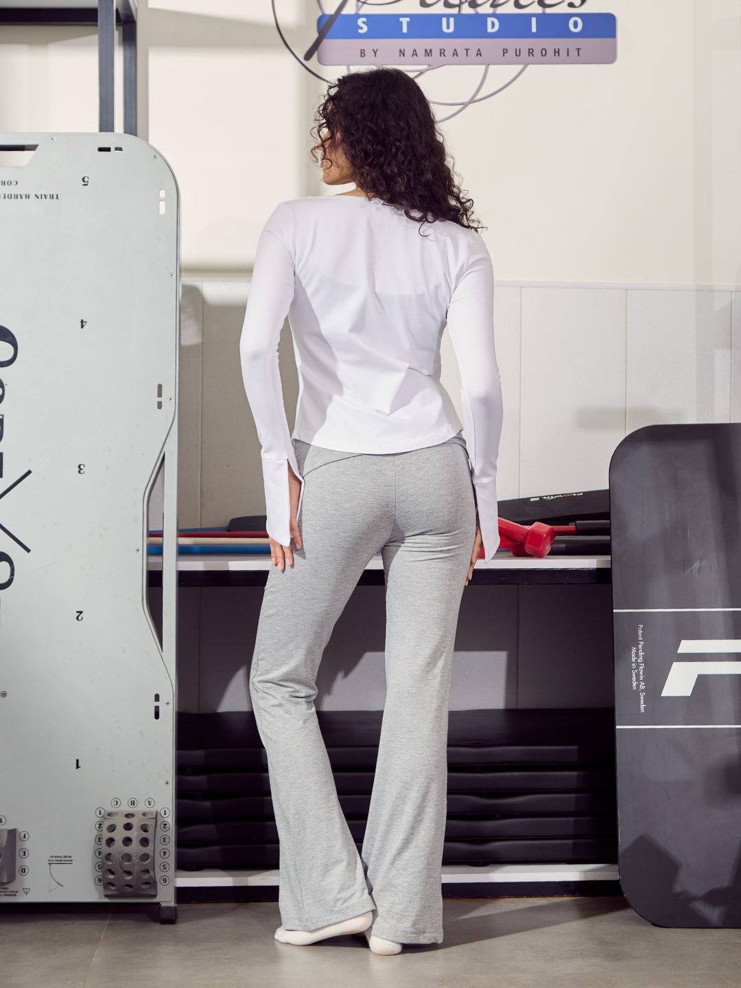Woman in white top and grey pants standing in a workshop with machinery.