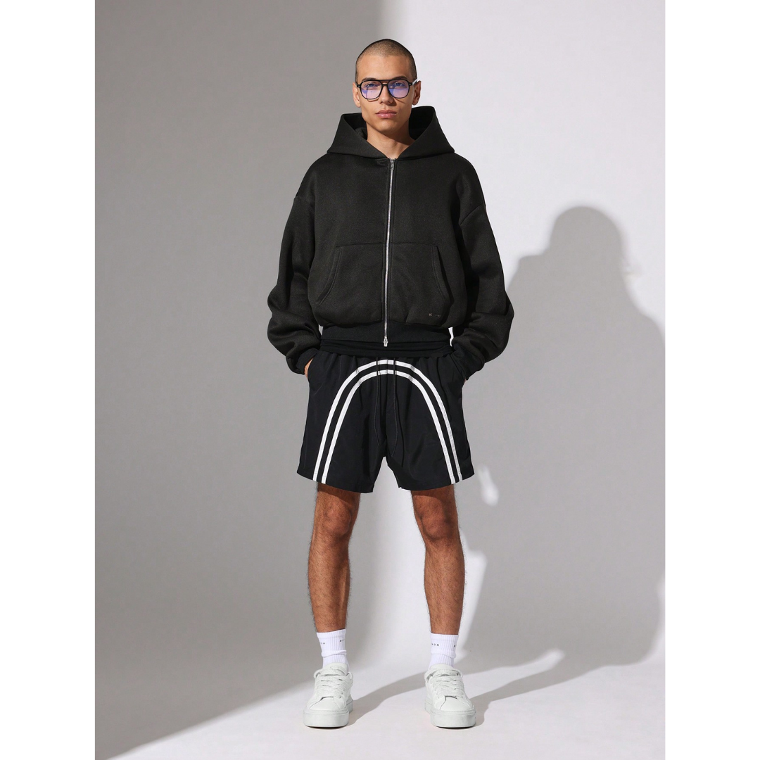 Person wearing a black hoodie and shorts with white stripes on a grey background