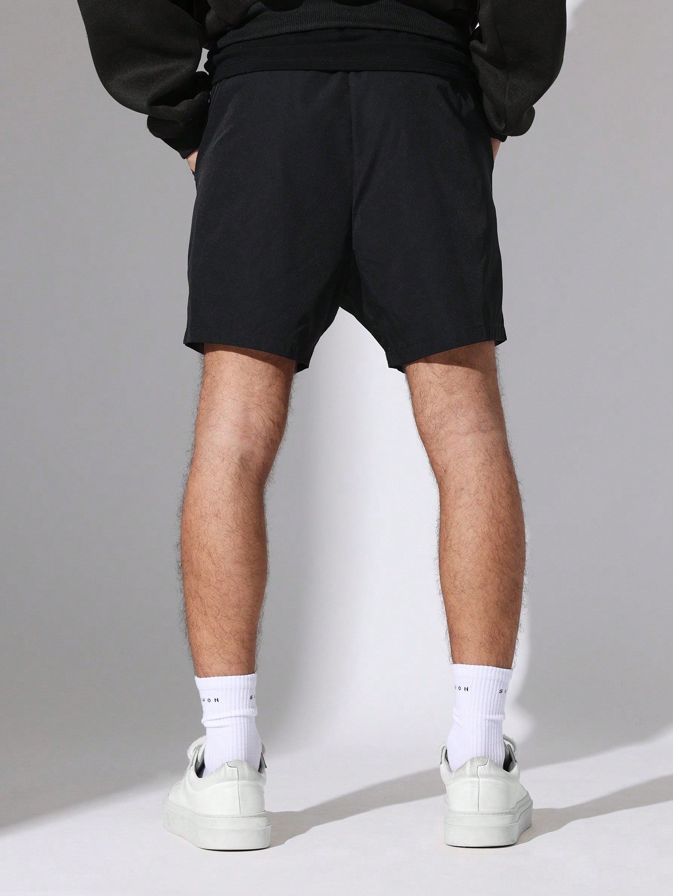 Person wearing black shorts and white sneakers on a plain background