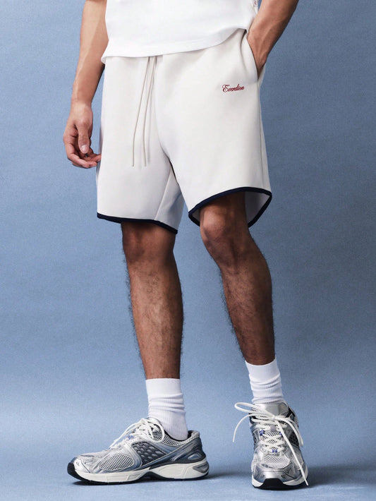 Person wearing white shorts with a logo and grey sneakers on a light blue background