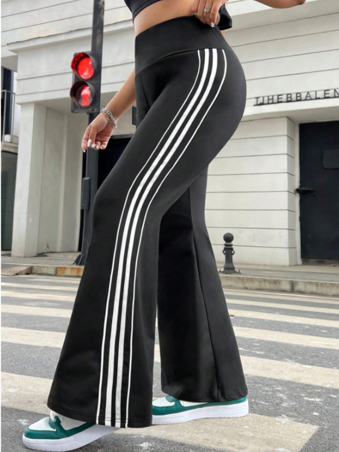 A model wearing black flare leggings with white stripes and a sports tee, standing on a crosswalk with a red traffic light in the background.