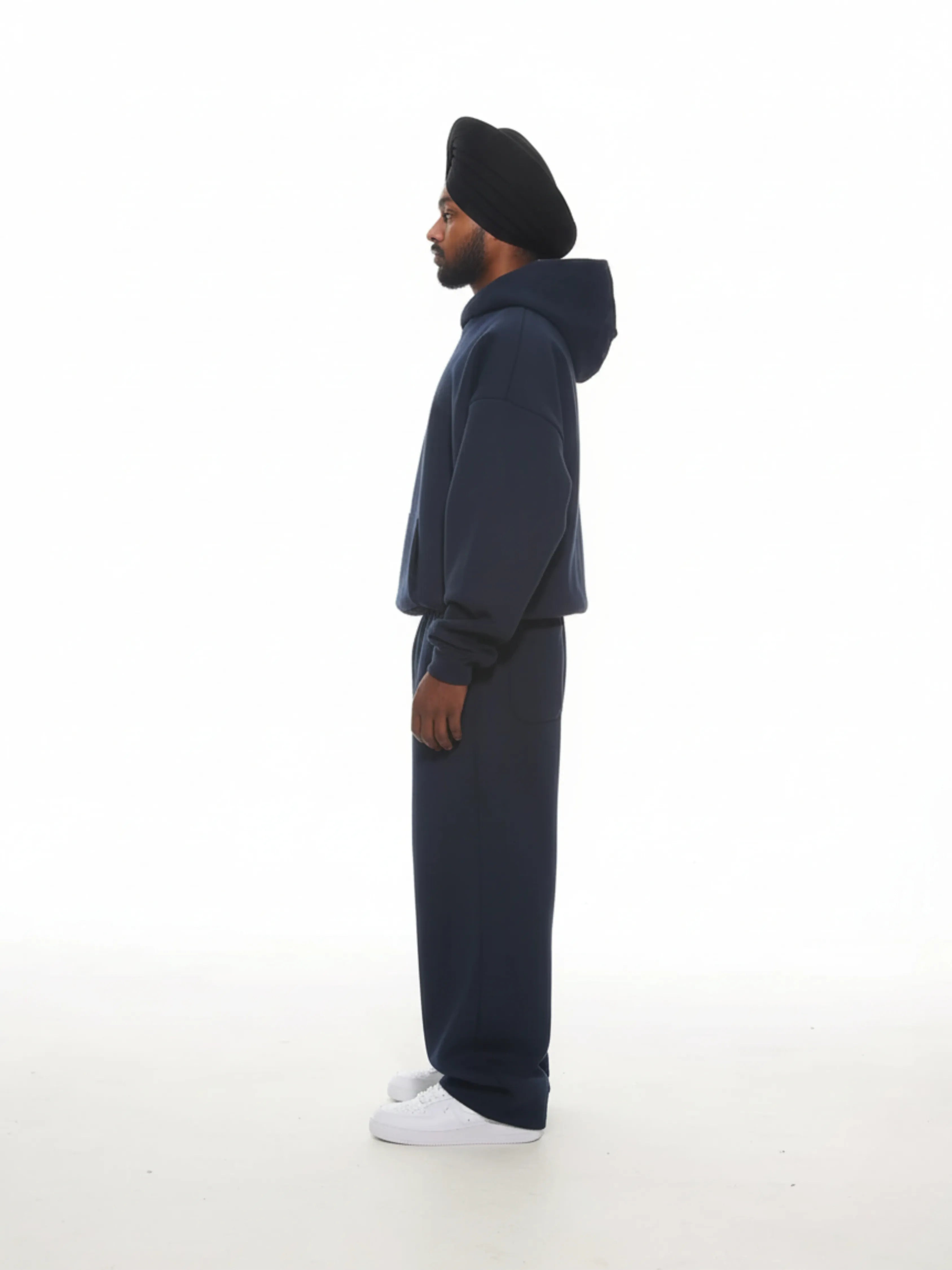 Person wearing a navy blue hoodie and pants with a black turban on a white background