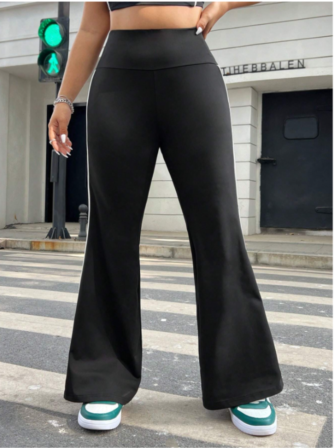 A model wearing black flare leggings with white stripes and a sports tee, standing on a crosswalk with a red traffic light in the background.