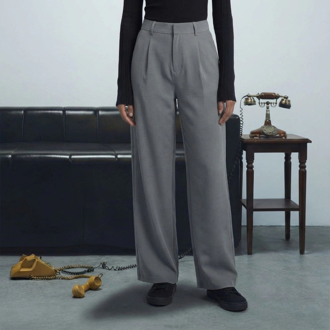 Person wearing gray trousers standing in a room with a black leather couch and vintage phone.