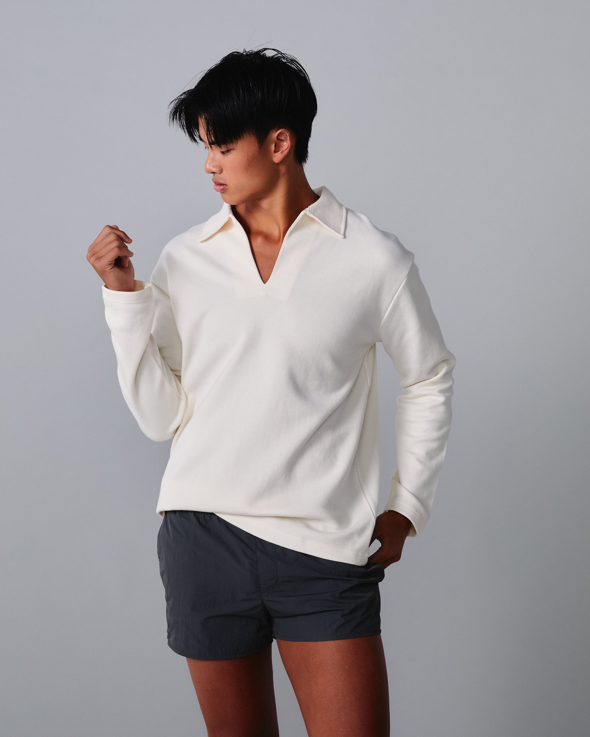 Person wearing a white long-sleeve shirt and dark shorts on a grey background